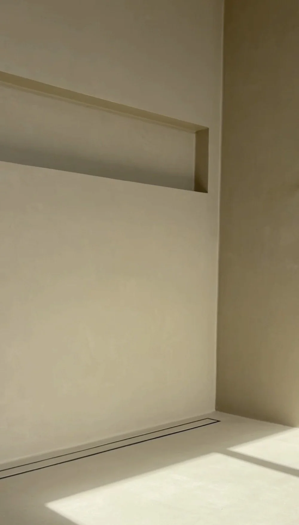 Warm neutral microcement shower with a recessed niche and linear drain