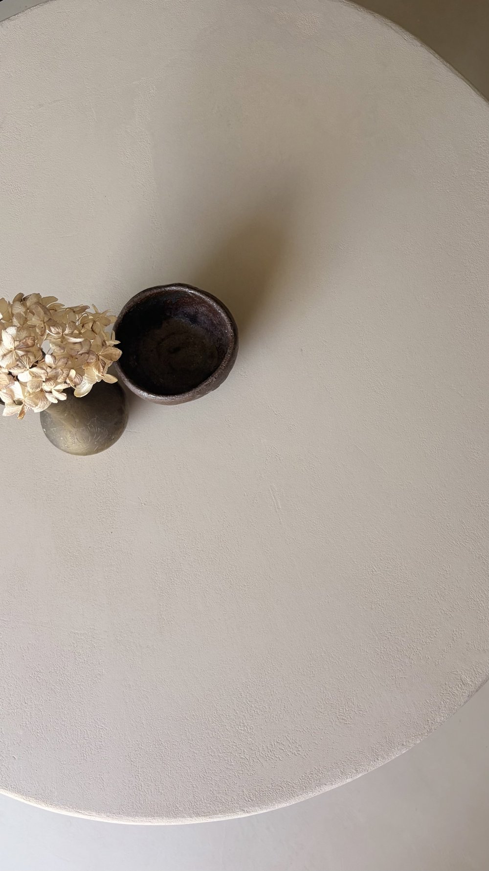 Close-up of a light neutral microcement tabletop with subtle texture and decorative vessels