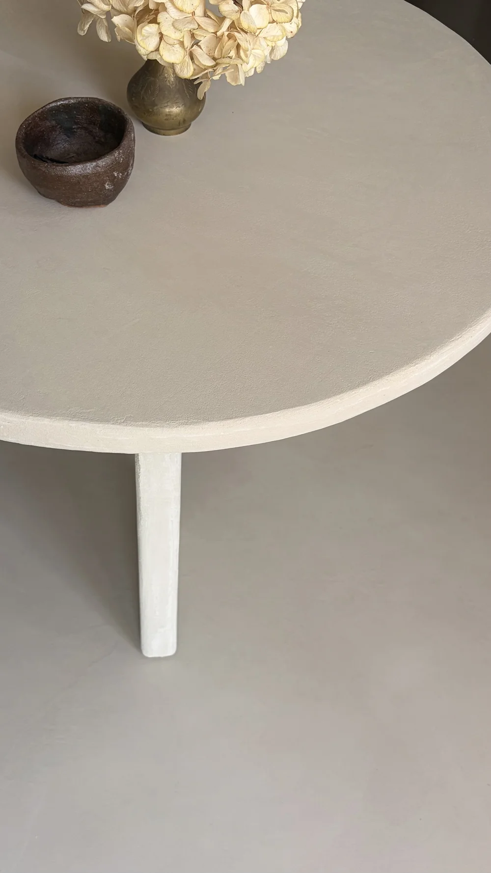 Light neutral microcement table styled with dried flowers and a ceramic bowl