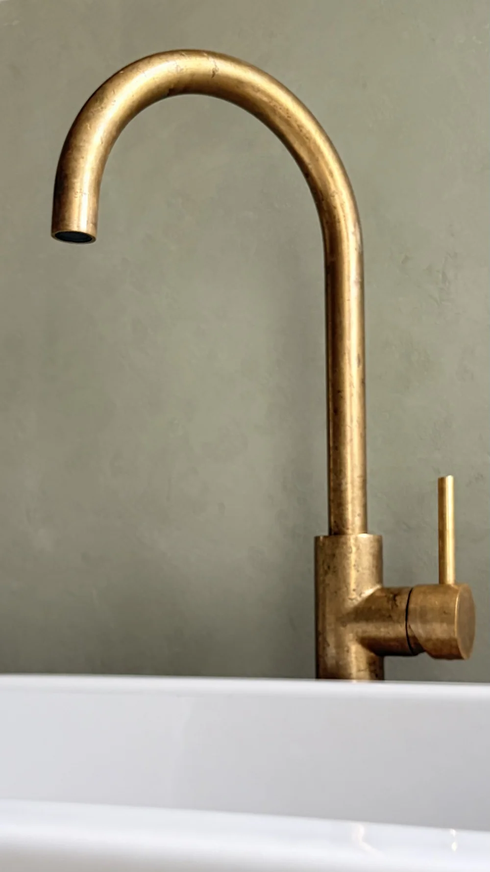 Curved brass basin tap against a softly textured microcement wall