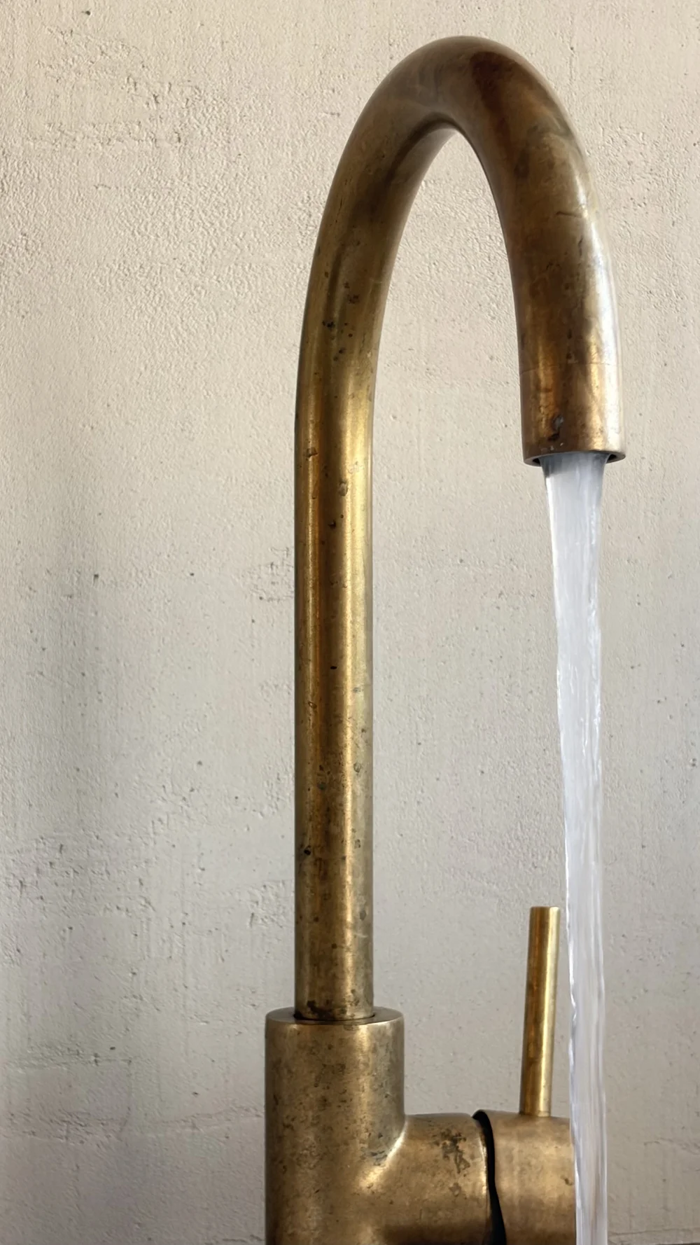 Water flowing from a curved brass tap beside a pale textured wall