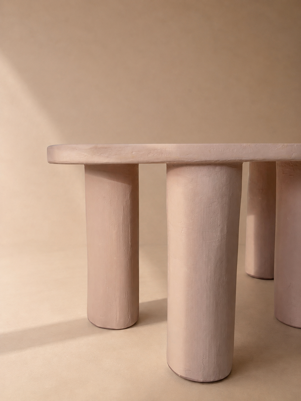 Close-up of a pink microcement table with rounded edge and cylindrical legs