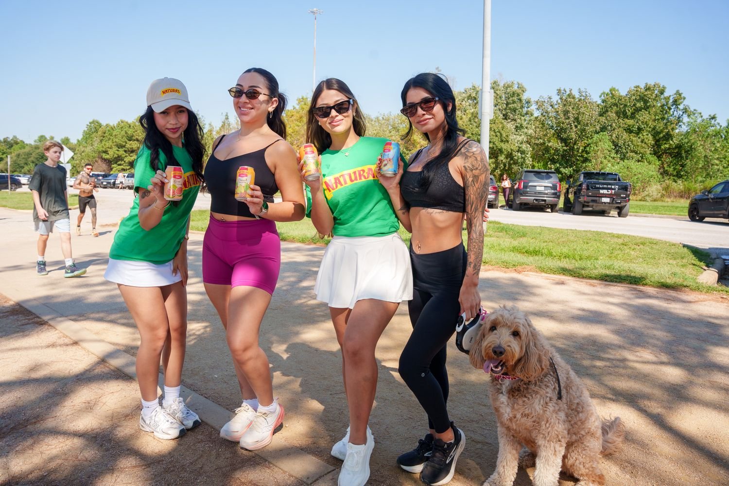 Two Naturas ambassadors posing with two event-goers and their dog, everyone holding a Naturas can