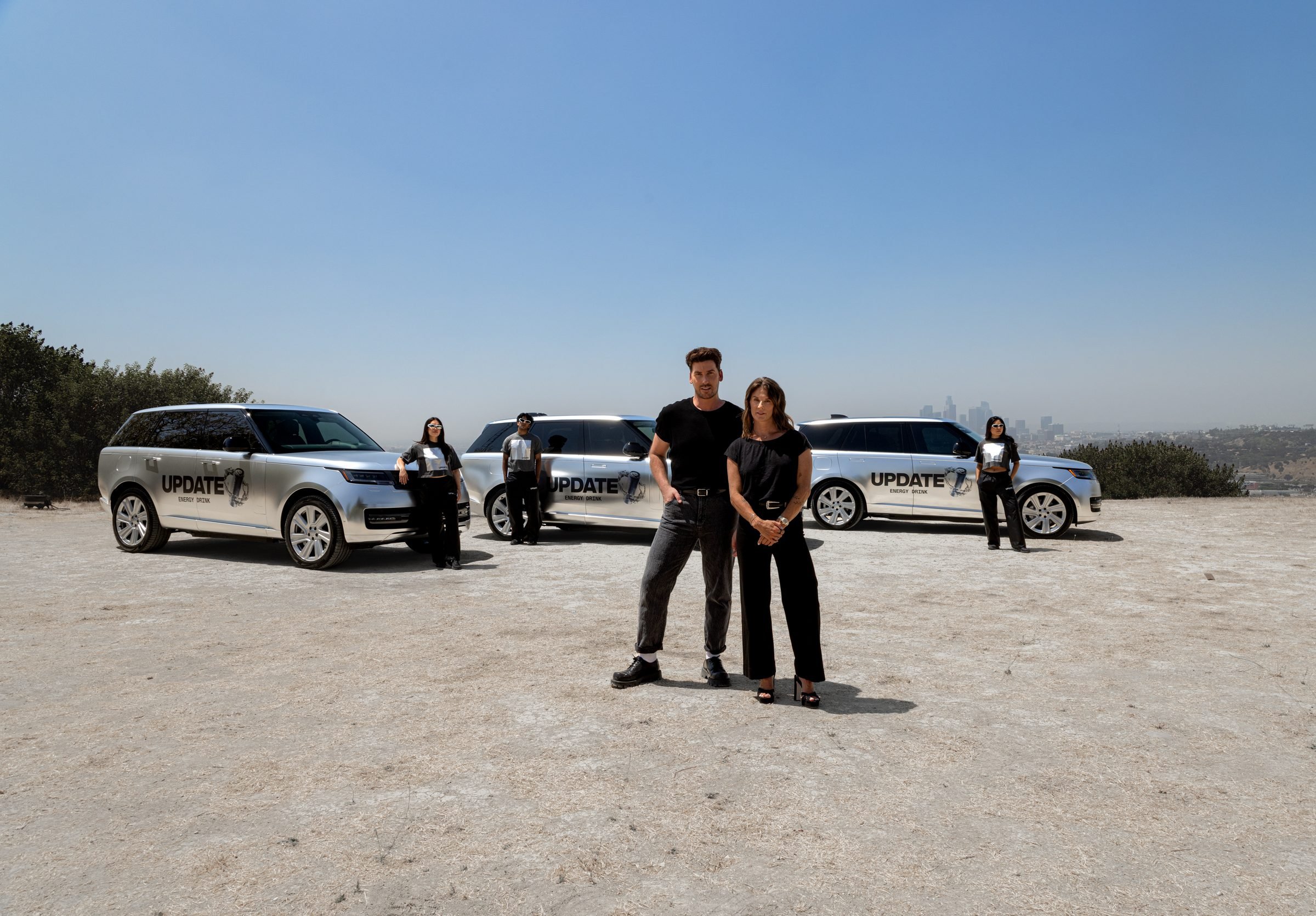 Two people standing in front of three UPDATE Energy Drink-wrapped Range Rovers with brand ambassadors on a hilltop above Los Angeles