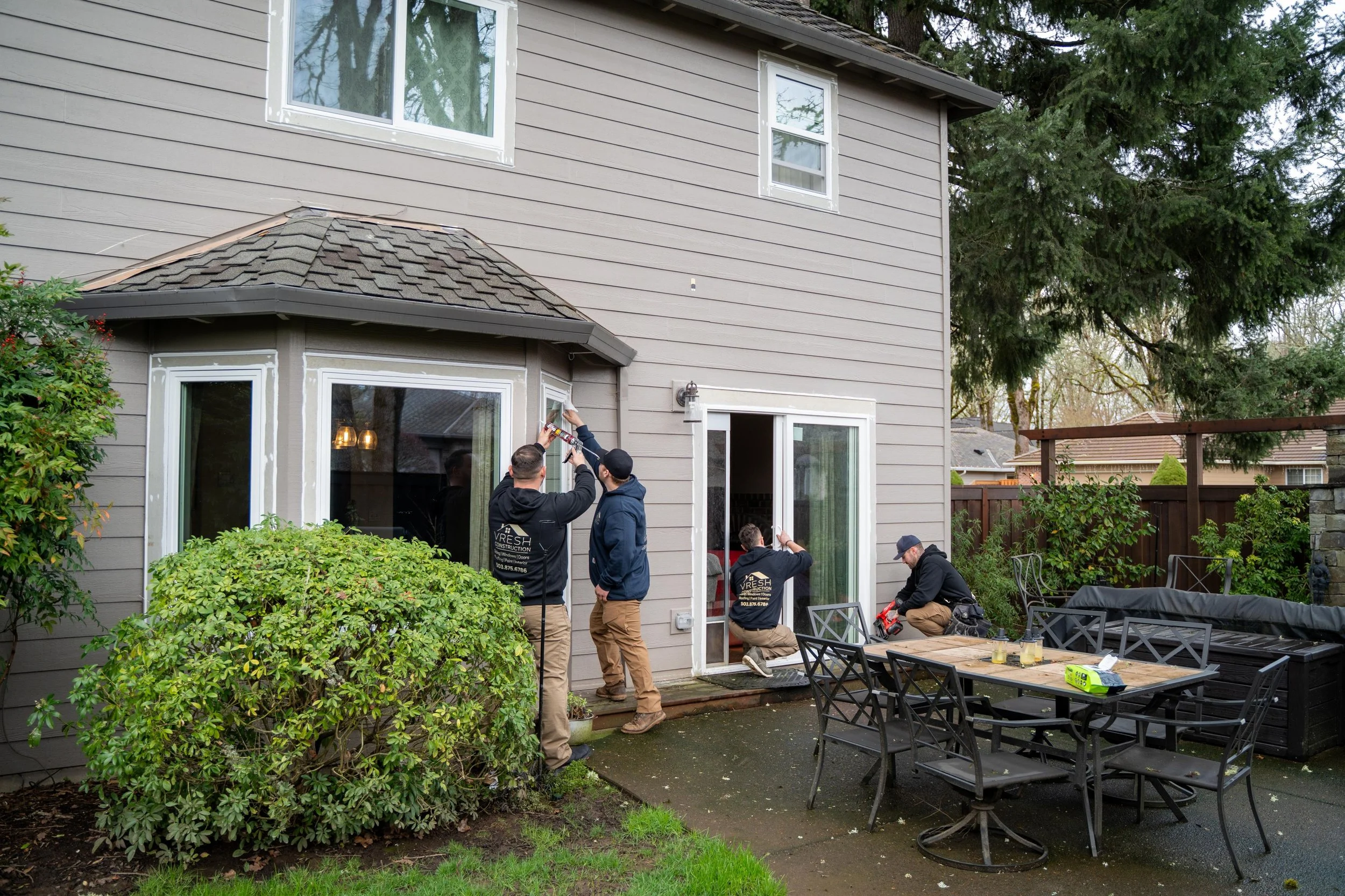 VResh Construction crew sealing the trim around a sliding patio door and bay window at the back of a Portland home