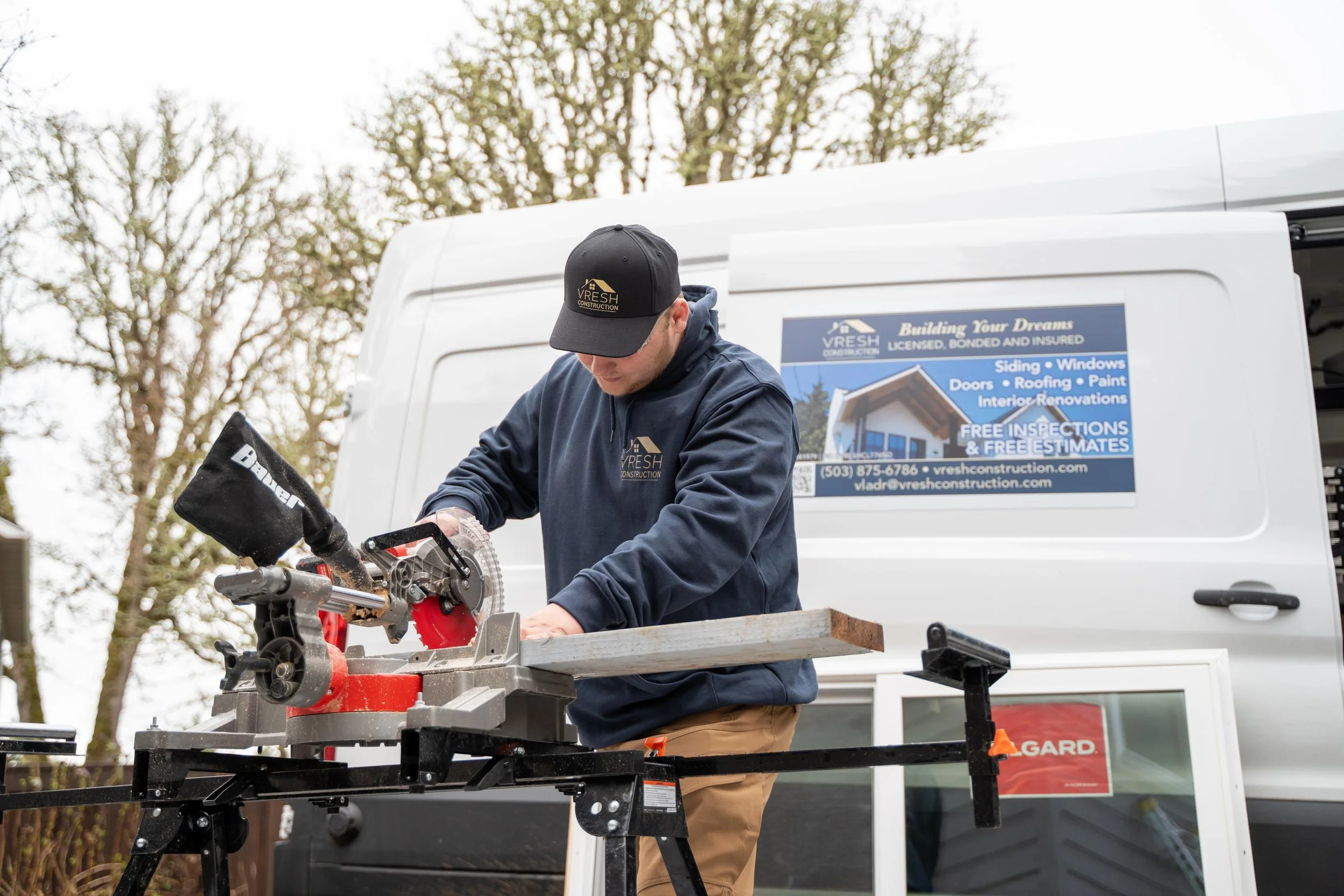 VResh Construction technician cutting window trim on a miter saw beside the van and a new Milgard window unit in Portland