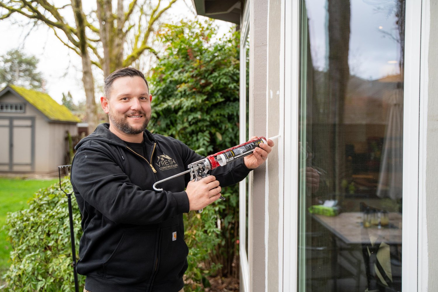 Vlad of VResh Construction sealing the frame of a sliding glass door on a Portland home