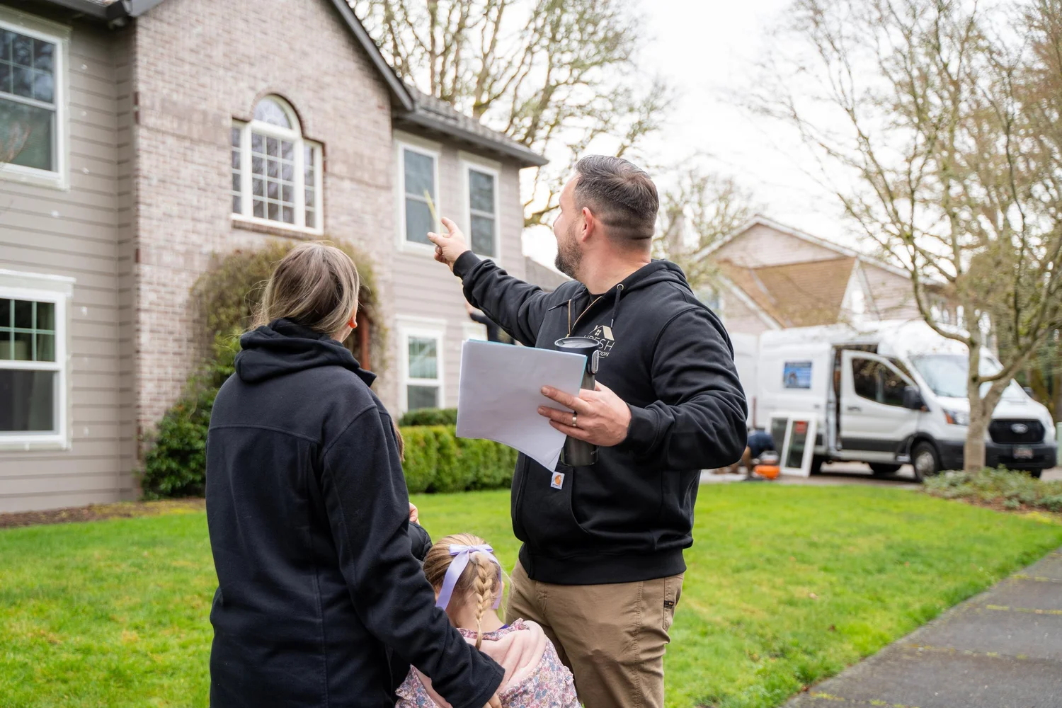 VResh owner holding a written estimate and pointing out windows to a homeowner and her daughter outside their home