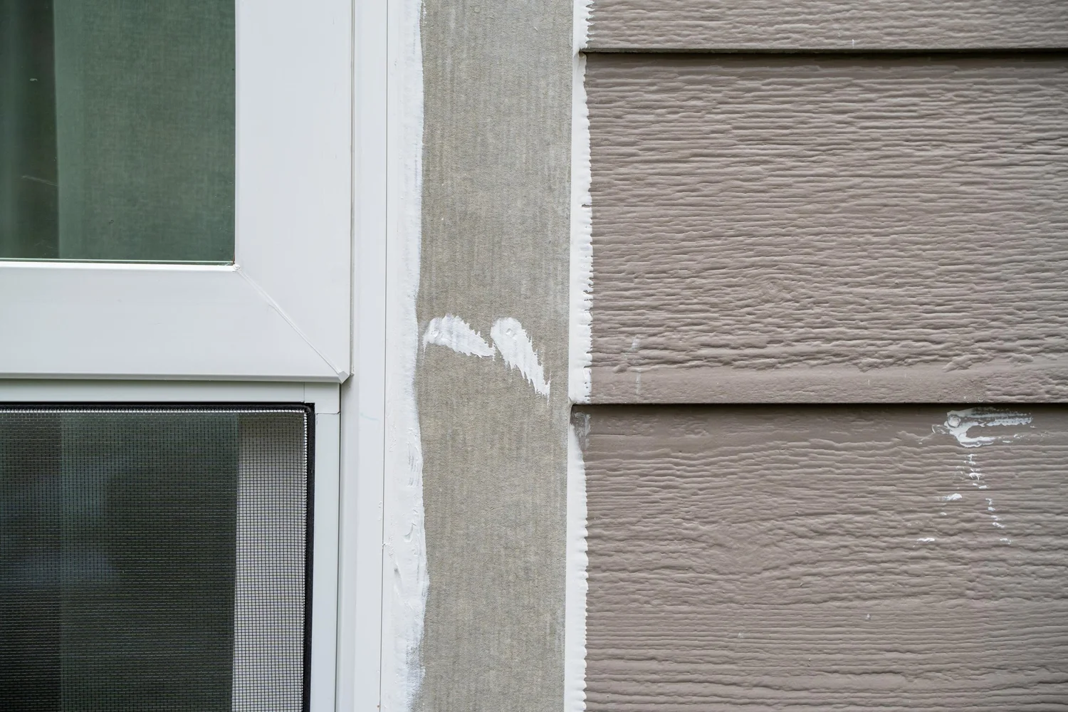 Close-up of a new white window frame set into fresh siding and trim, showing the jamb and trim detail