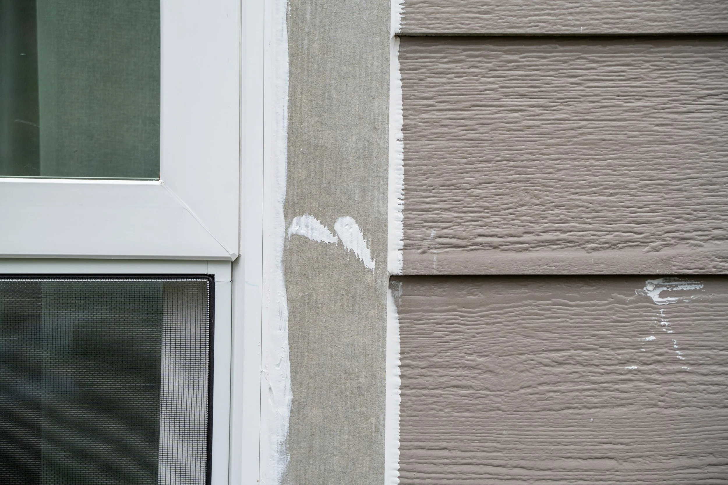 Close-up of new white trim and fresh caulk where a frame meets grey lap siding, for VResh Construction exterior door repair in Washougal, WA