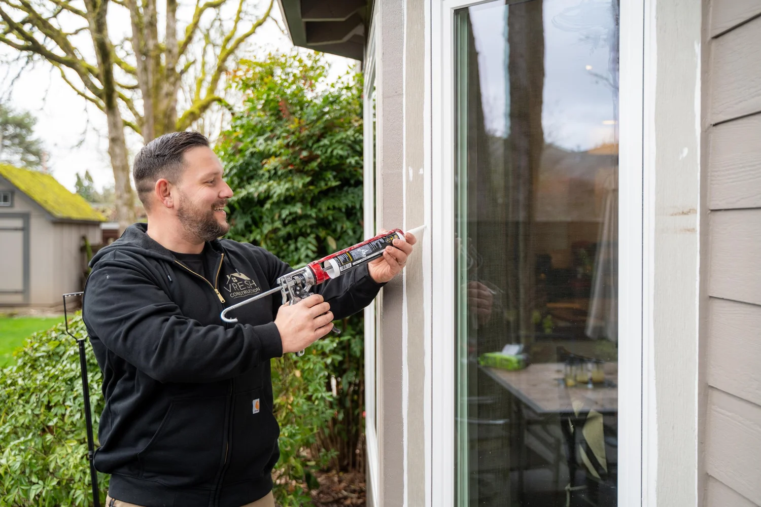 Vlad of VResh Construction sealing the frame of a sliding glass door with a caulk gun