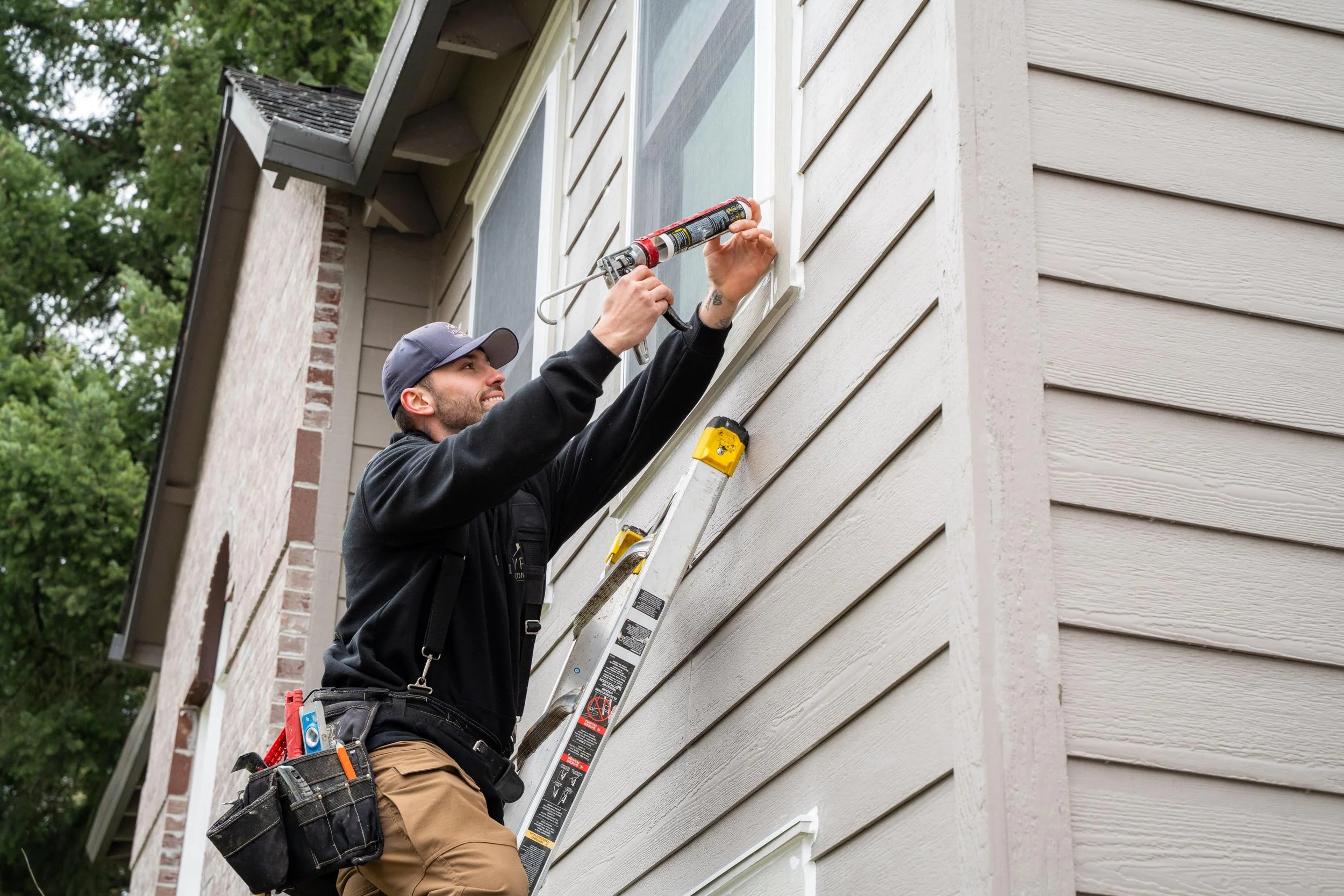 VResh Construction technician on a ladder fitting trim at an upper window of a Portland home