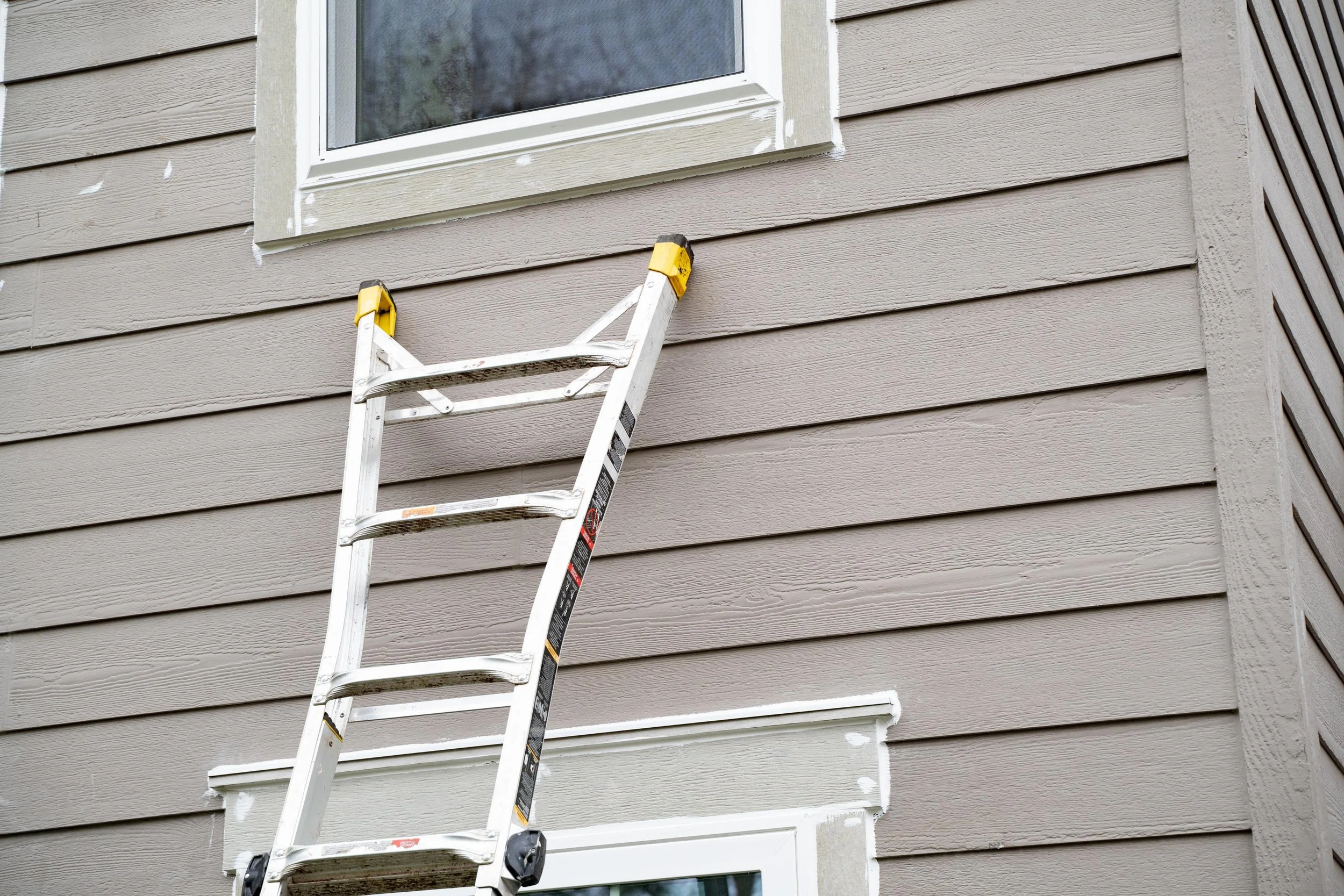 Ladder set against the siding below a window of a Portland home during a VResh window installation