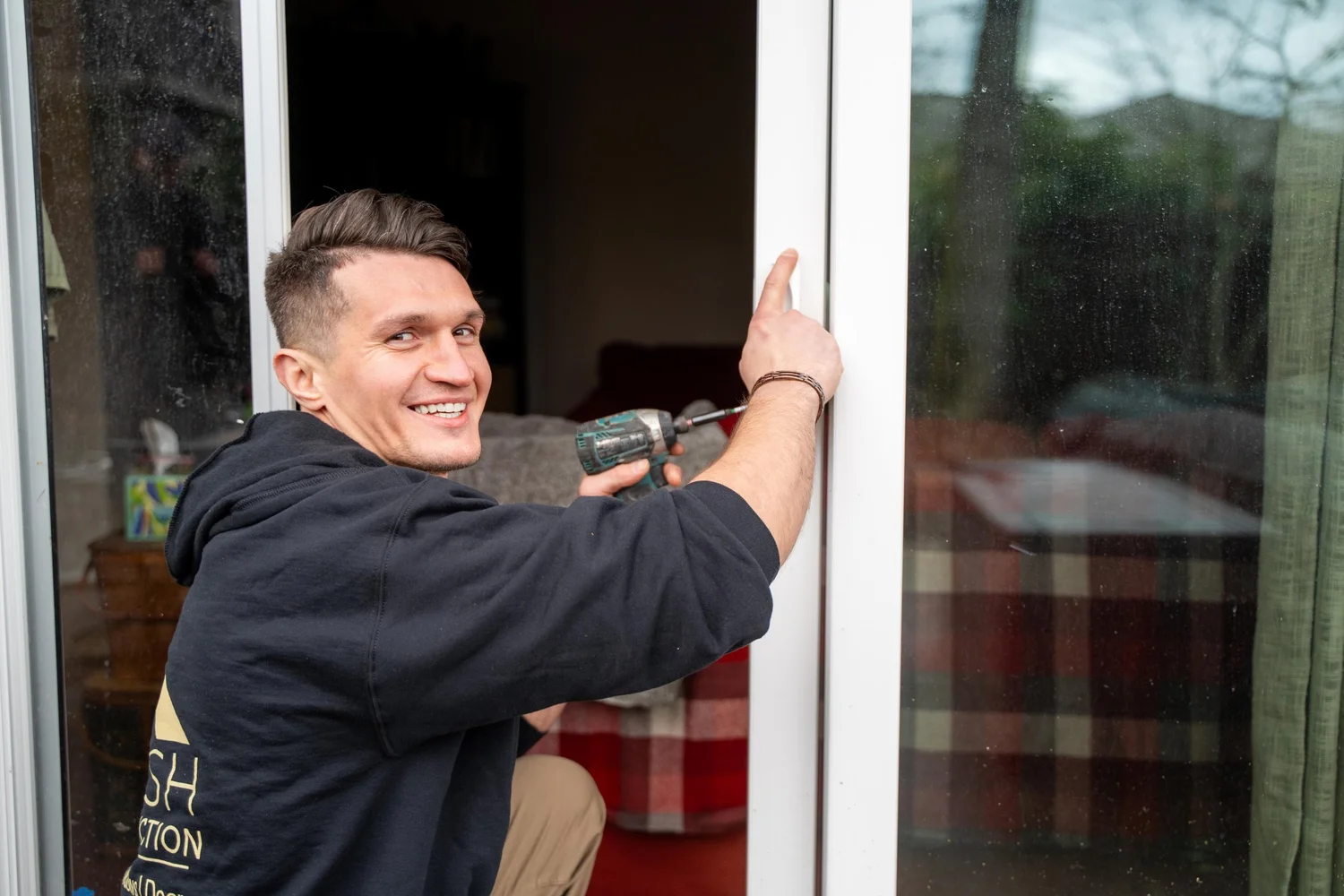 A smiling VResh Construction carpenter fastening the frame of a sliding glass door with a cordless drill