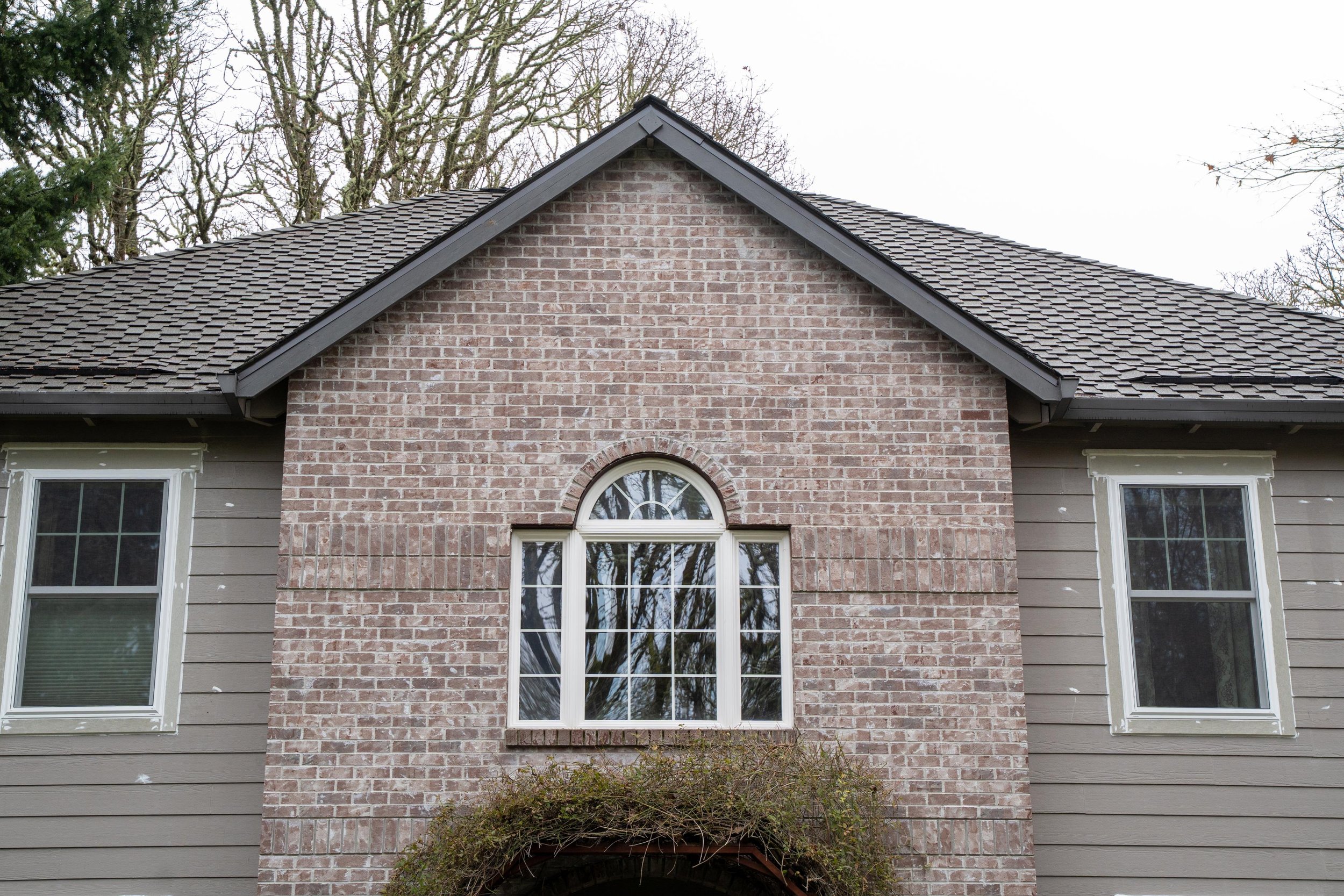 Front gable of a grey brick Portland home with a large arched-top window framed in white