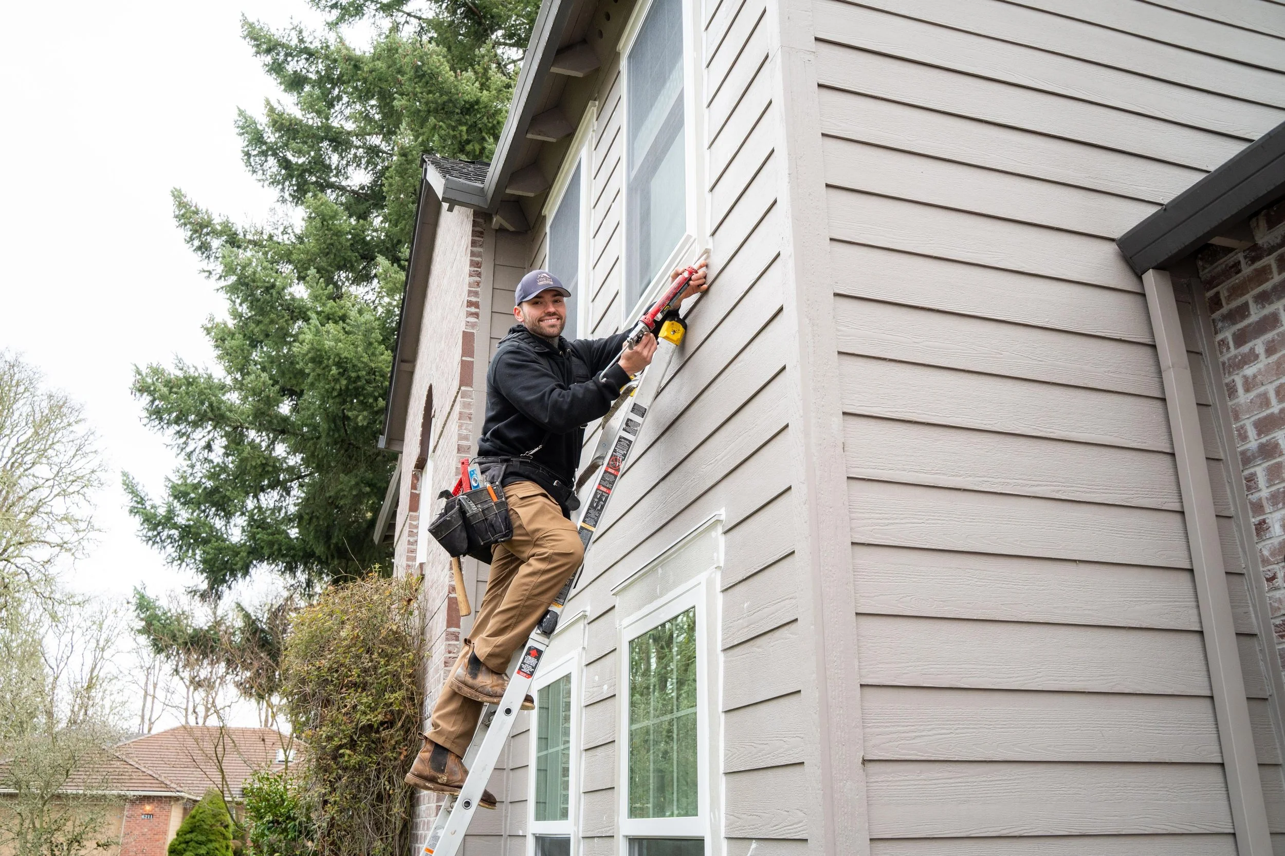 VResh Construction technician on a ladder working at an upper window of a Portland home during a window replacement