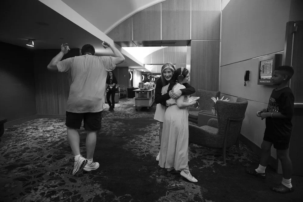 Christine embraces Jadyne, who wears headphones, as Luke stands to the left.