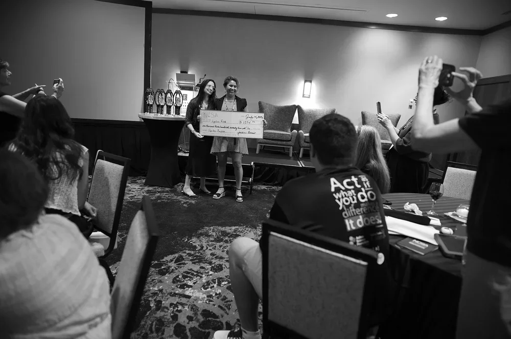 Jackie presents a ceremonial NCSA grant check to Lydia Rios on stage.