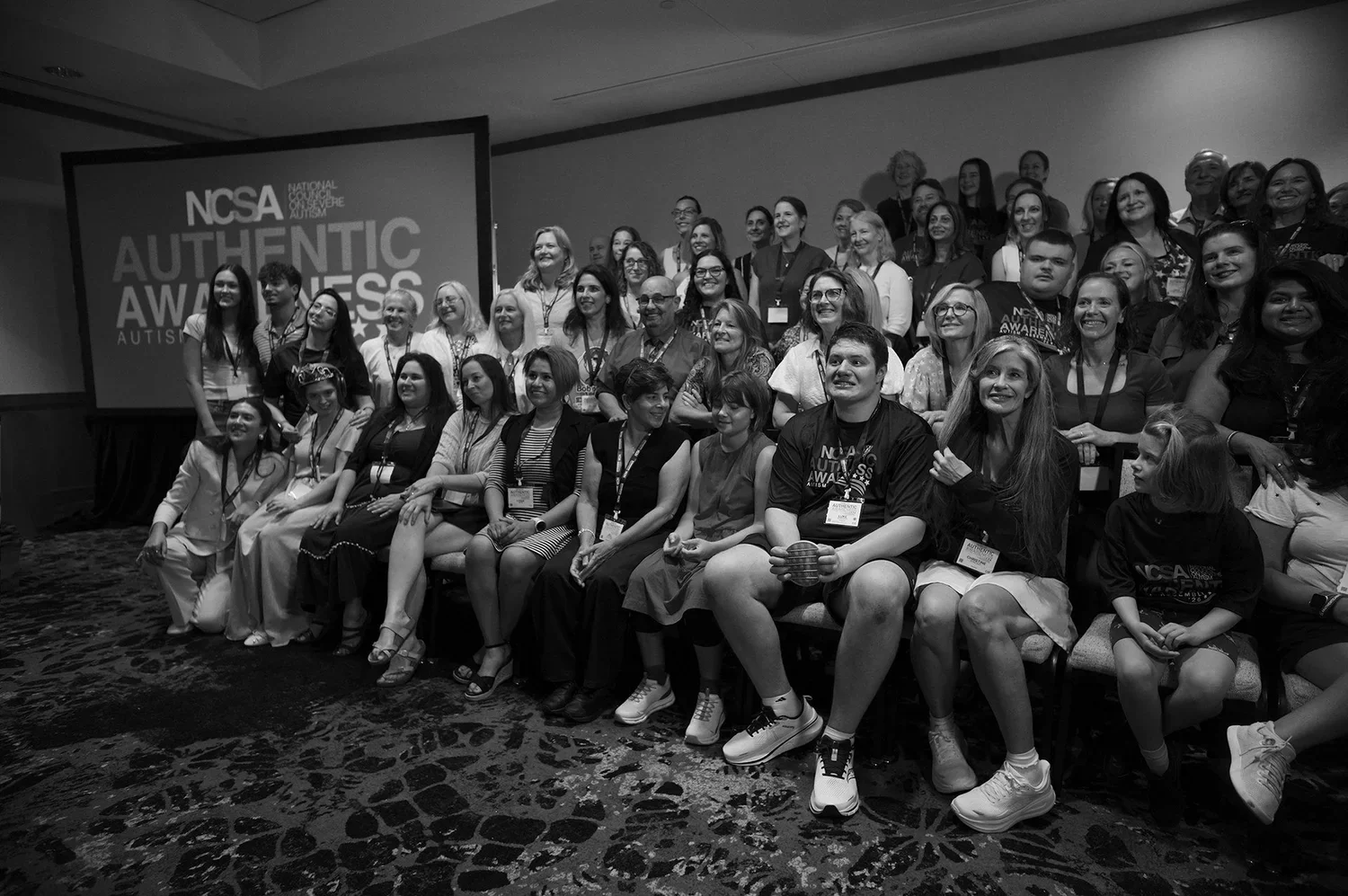 The full NCSA delegation gathered for a group portrait in front of a screen reading NCSA Authentic Awareness, families and young adults seated together.