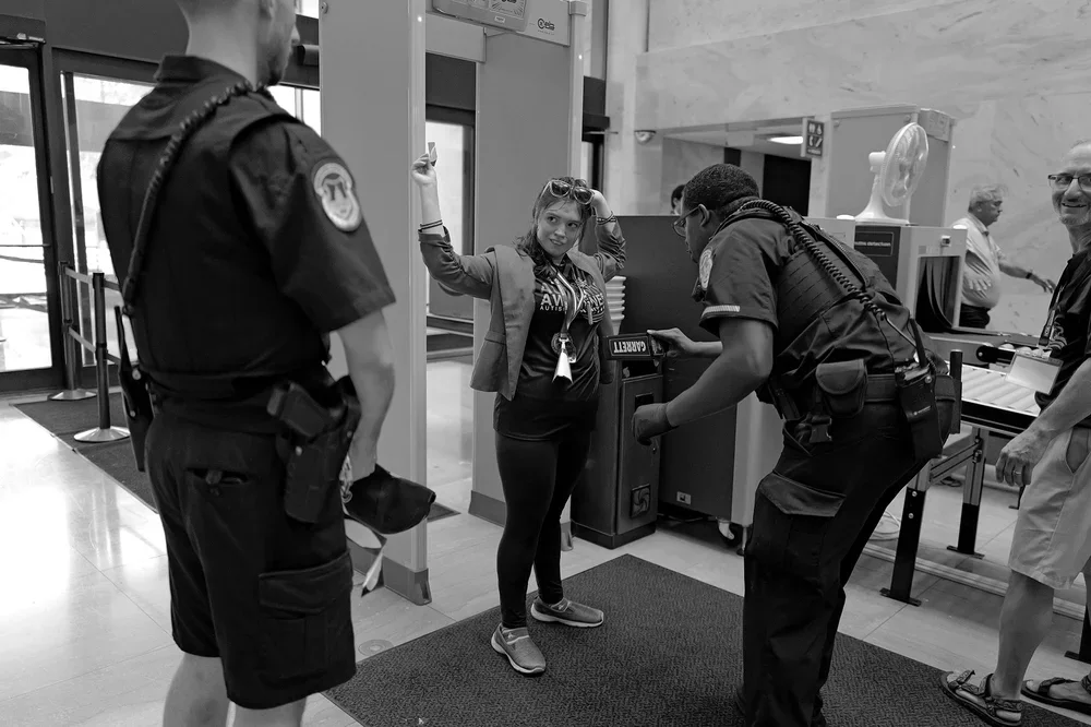 Jadyne smiles as an officer runs the security wand past her raised badge.