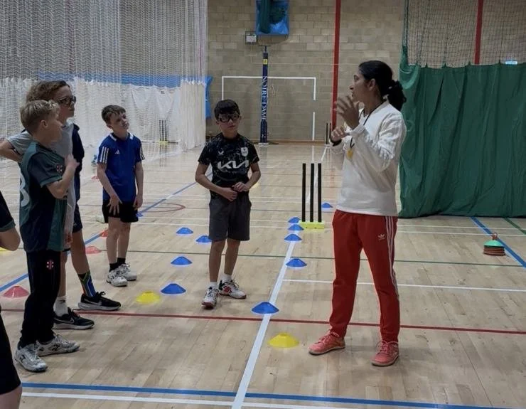 Shashi demonstrating a coaching point to a small group of junior cricketers in an indoor sports hall
