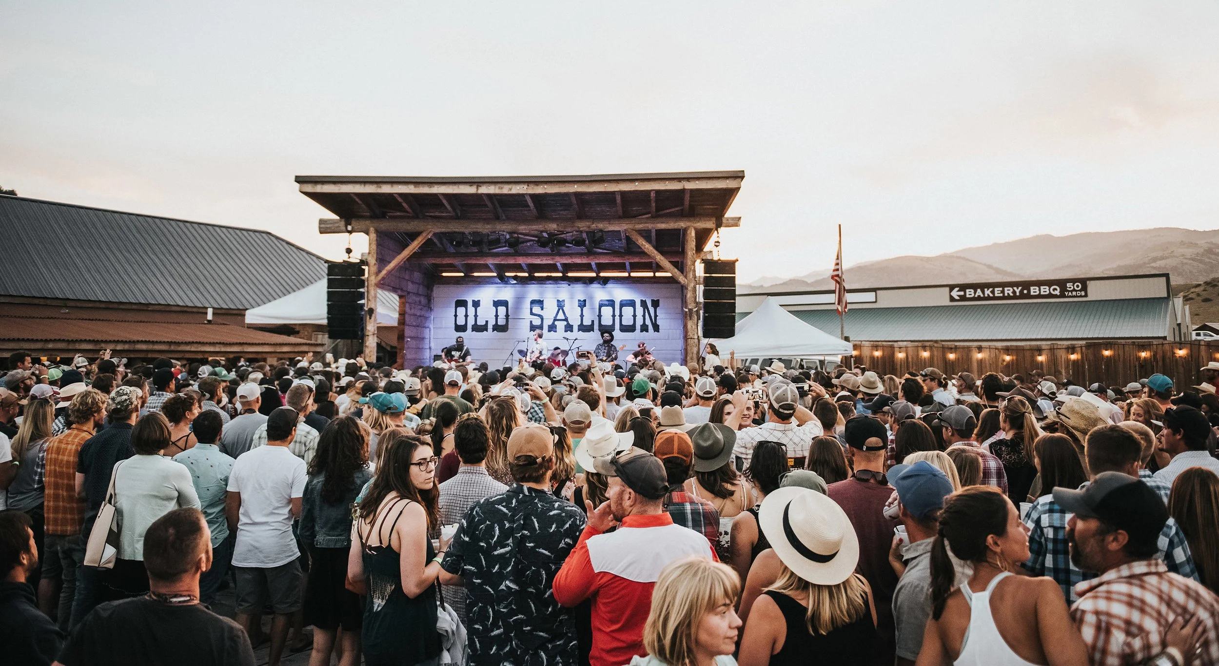 A crowd in cowboy hats watching a band on the outdoor Old Saloon stage