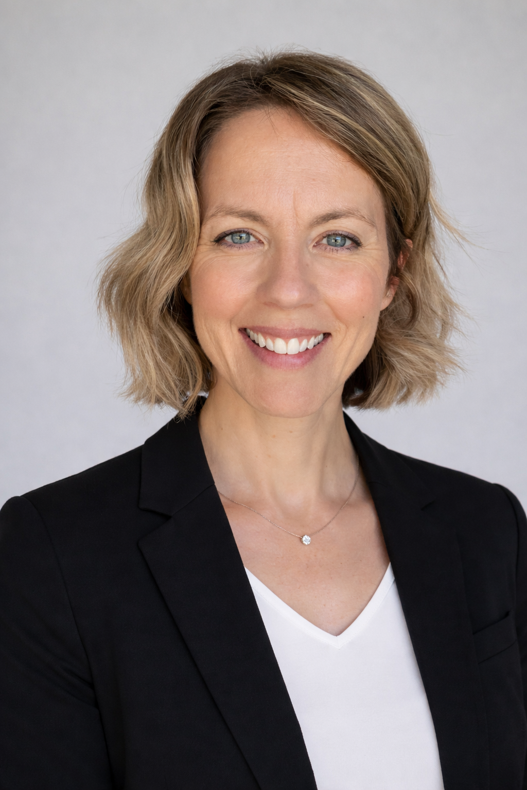 Sarah Chatfield smiling in a black blazer and light top against a pale background.