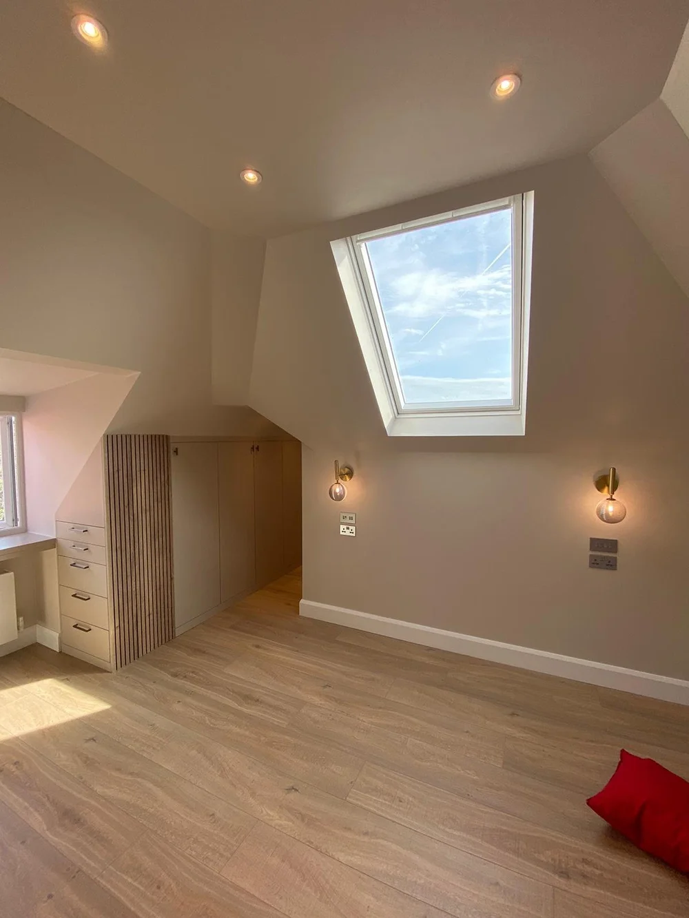 Loft bedroom with a roof window and wall lights in a Wimbledon loft conversion by RELM Interiors