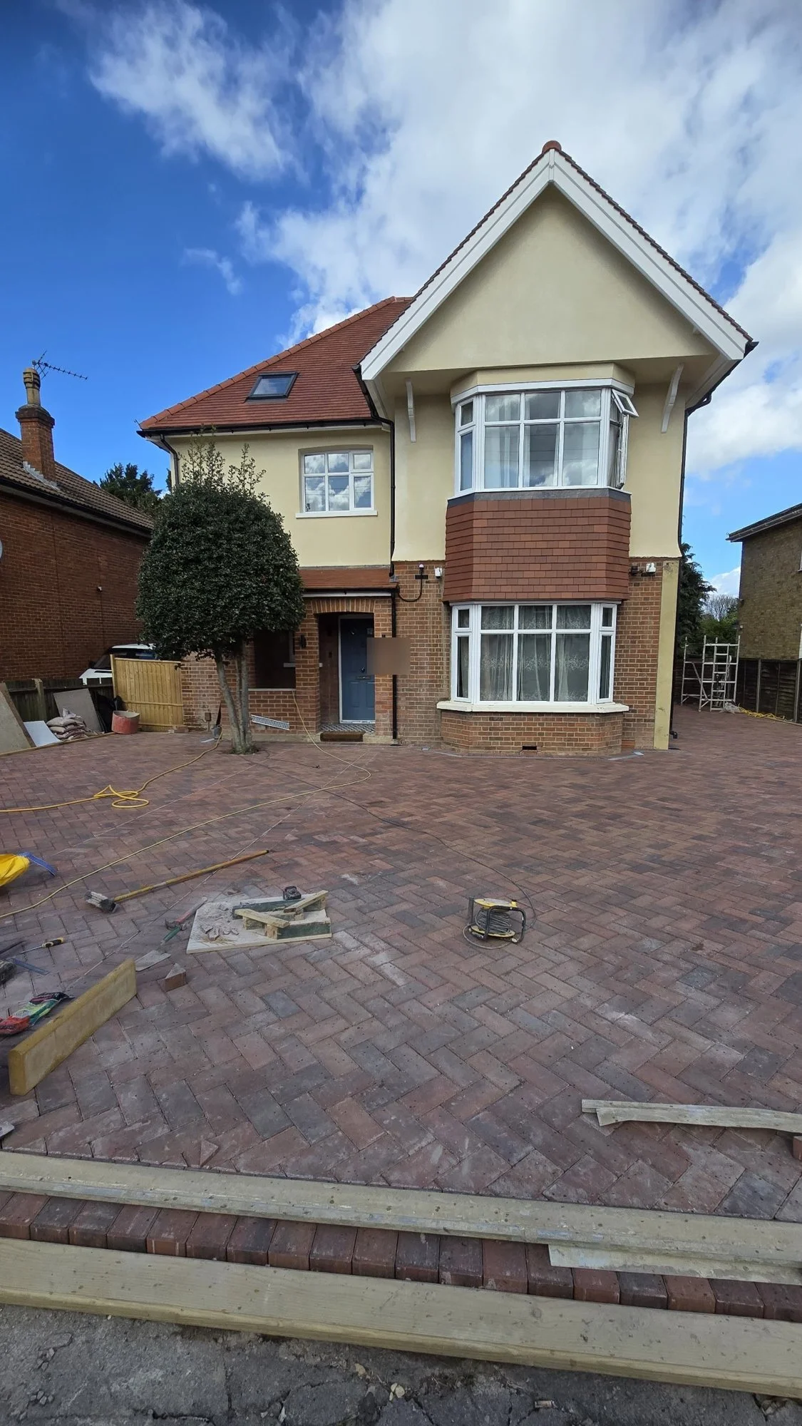 Rendered front of a Wimbledon family house with a new red clay tile roof and herringbone block driveway, renovated by RELM Interiors