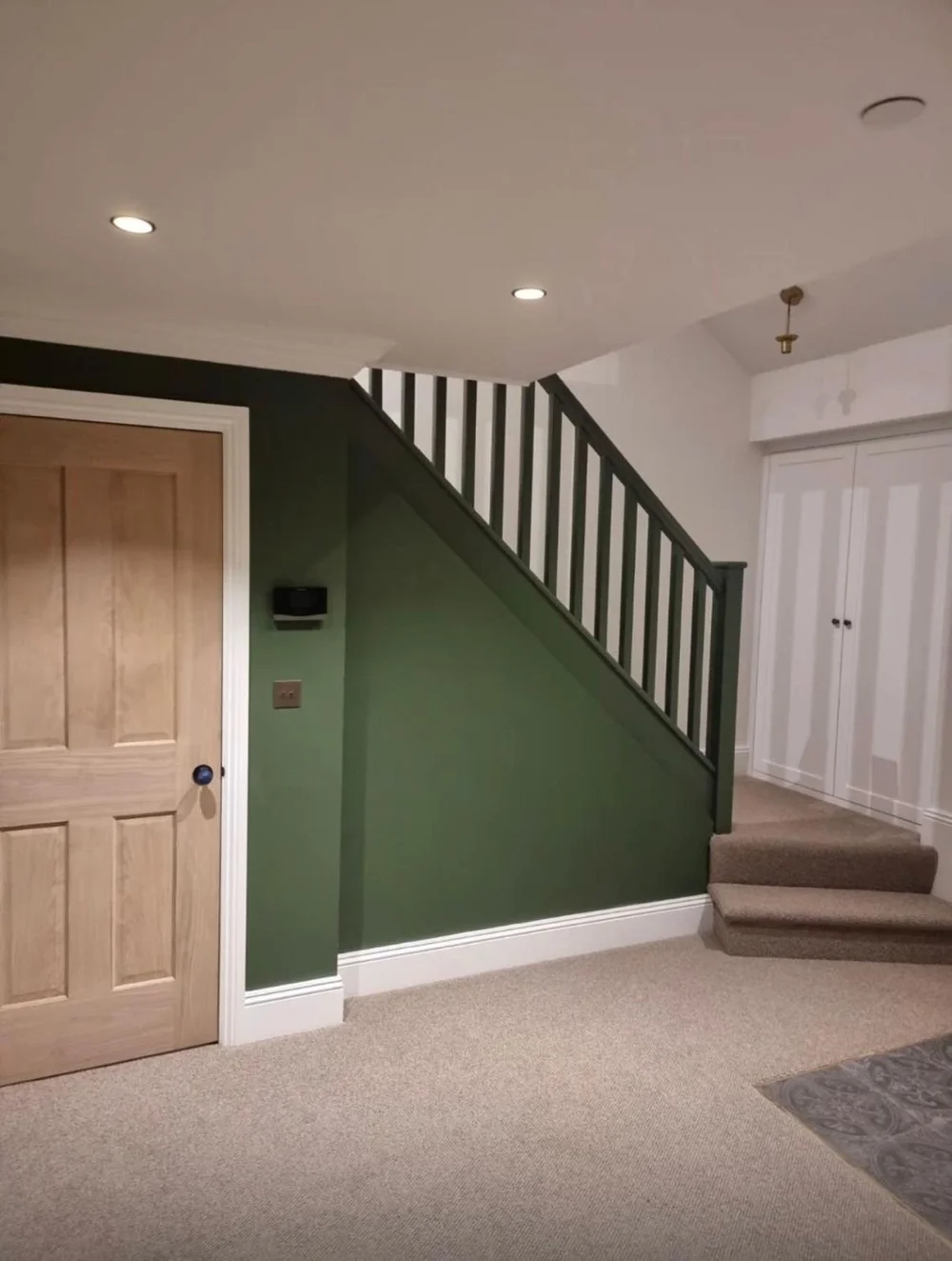 Green hallway with a painted staircase, oak door and wool carpet in a Victorian cottage in SW19