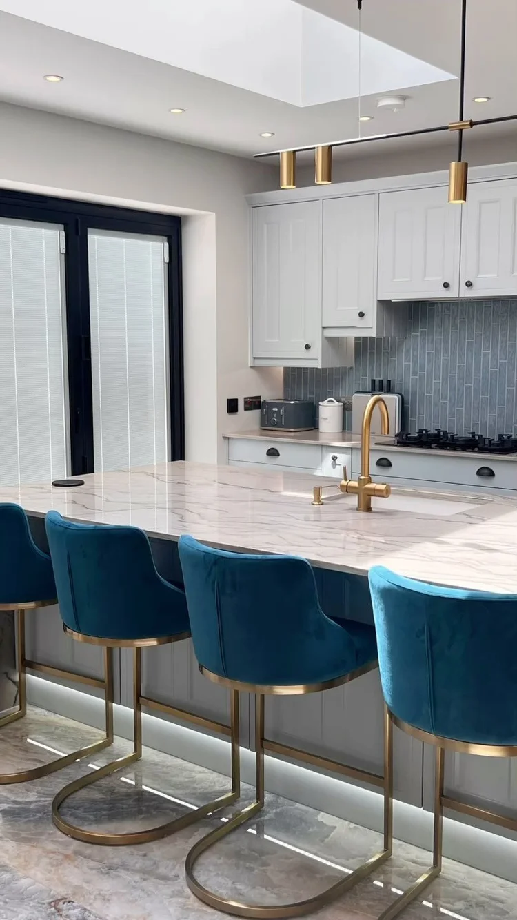 Stone kitchen island with brushed-brass tap and blue velvet bar stools