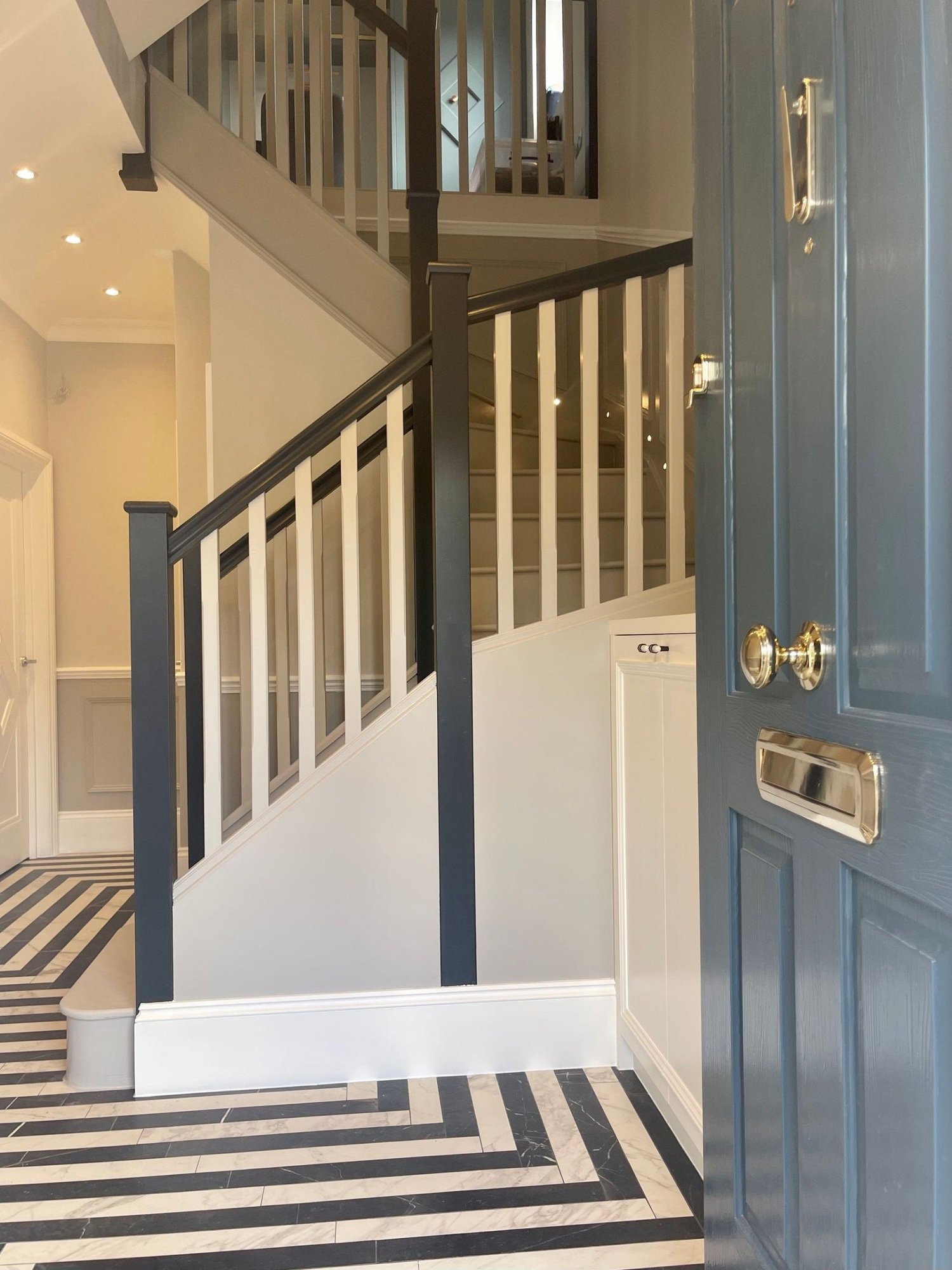 Hallway with painted staircase, black-framed glass screen and marble chevron floor