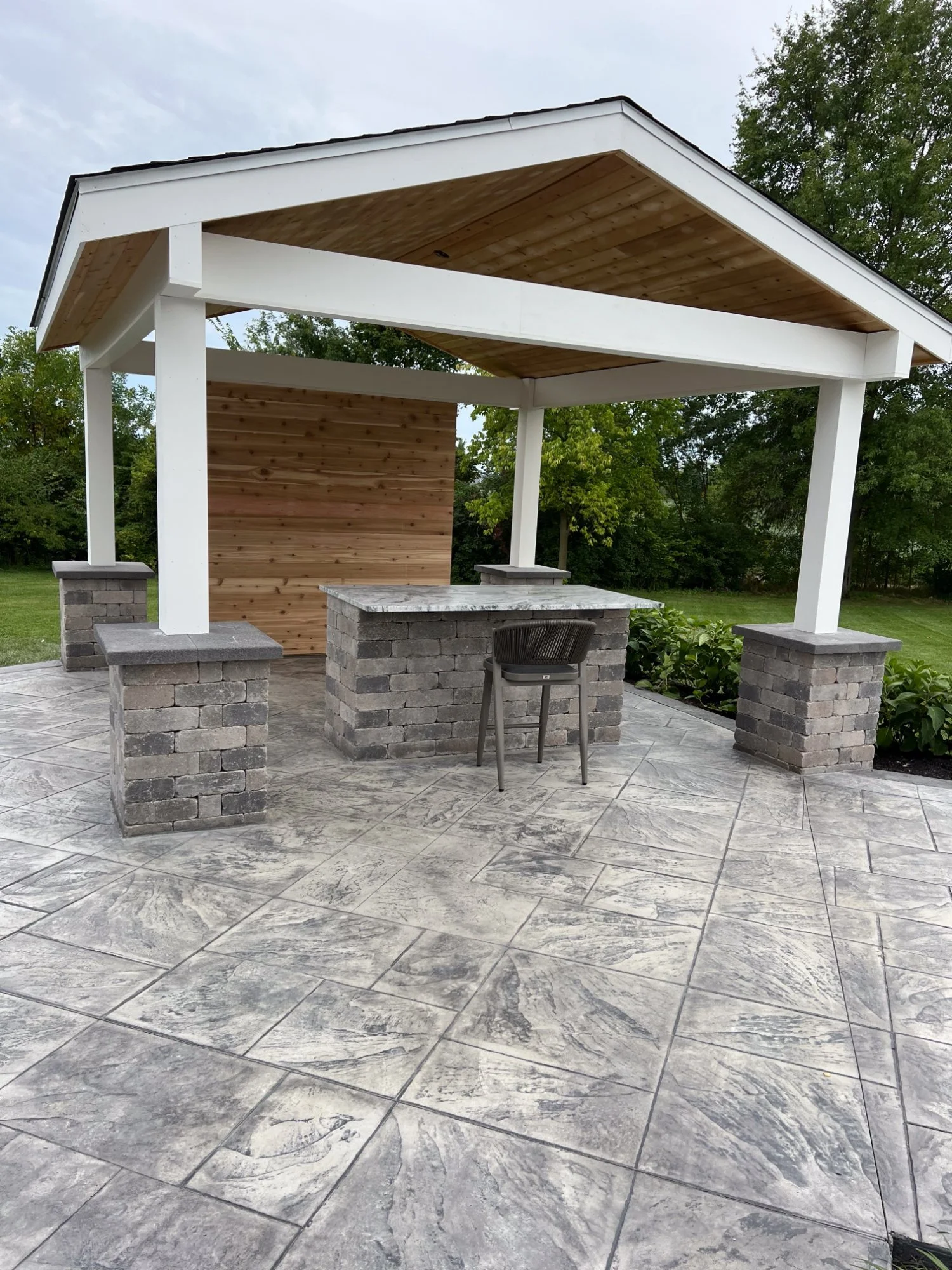 White gable pavilion with stamped concrete and stone outdoor kitchen