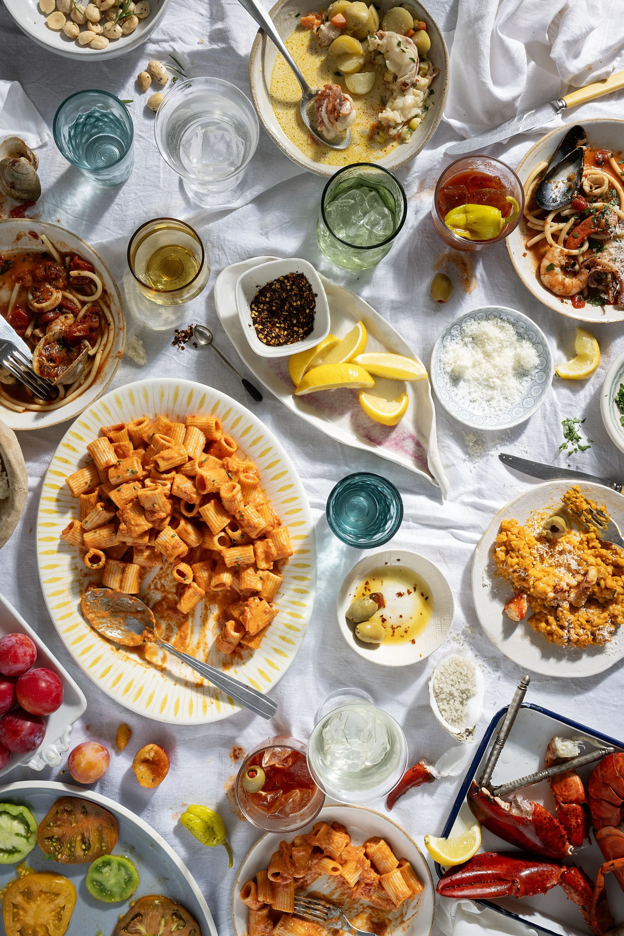 Overhead coastal meal with lobster, pasta, and cocktails