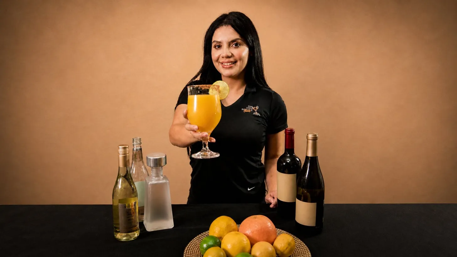 On The Rocks Girls bartender in a branded OTR polo holding out a fresh citrus cocktail at an event bar