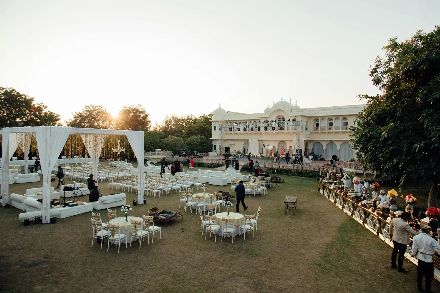 Grand outdoor wedding ceremony with floral arch and long reception tables at golden hour
