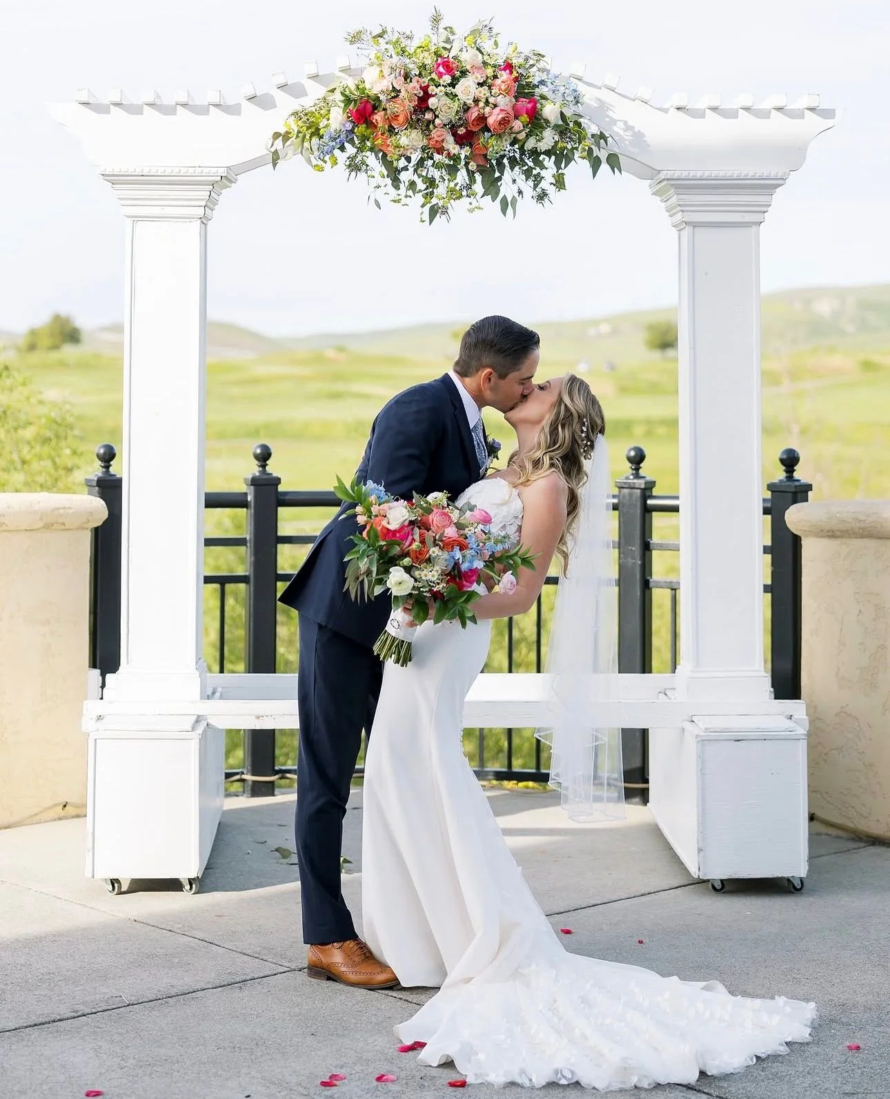 Claire and Mitch under a floral pergola with rolling hills behind