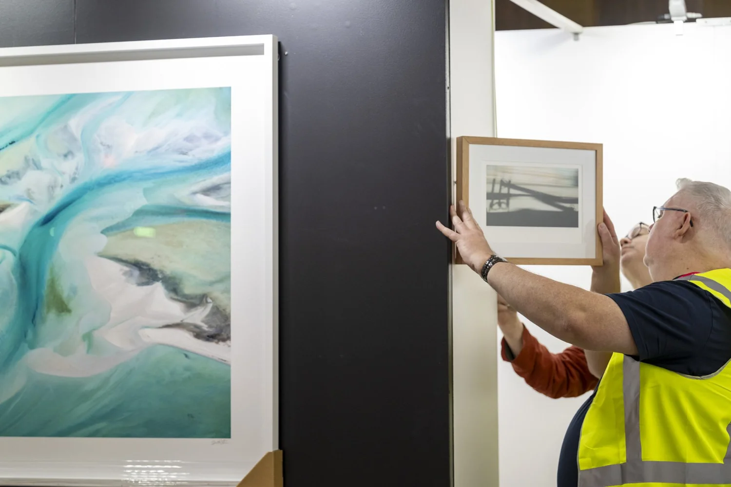 An IRID installer hanging a framed photograph beside the black feature wall
