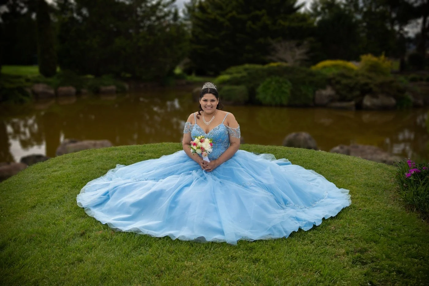 Milestone portrait of a young woman in a blue gown beside a garden pond