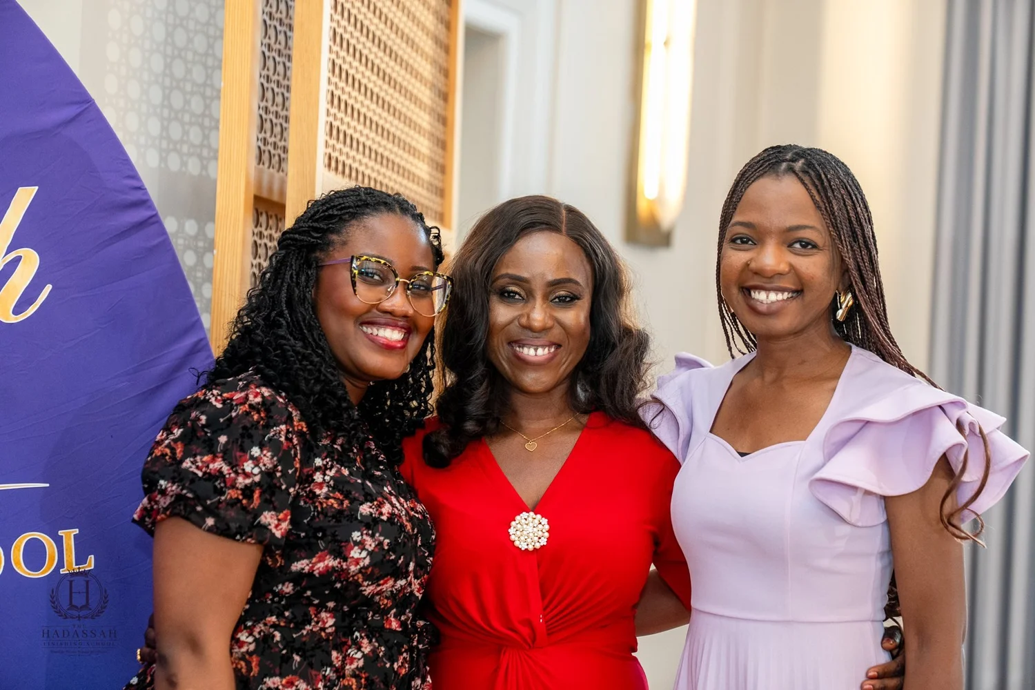 Three attendees smiling together in front of the event backdrop