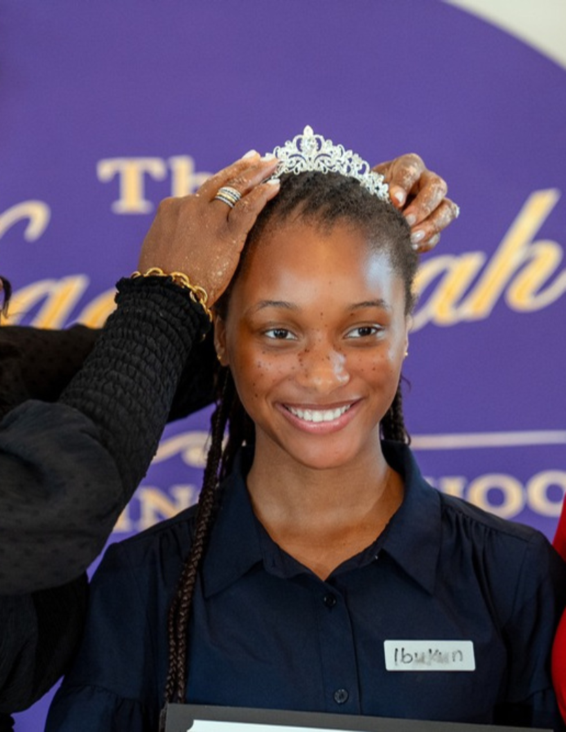 A participant smiling as a crown is placed on her head at the closing ceremony