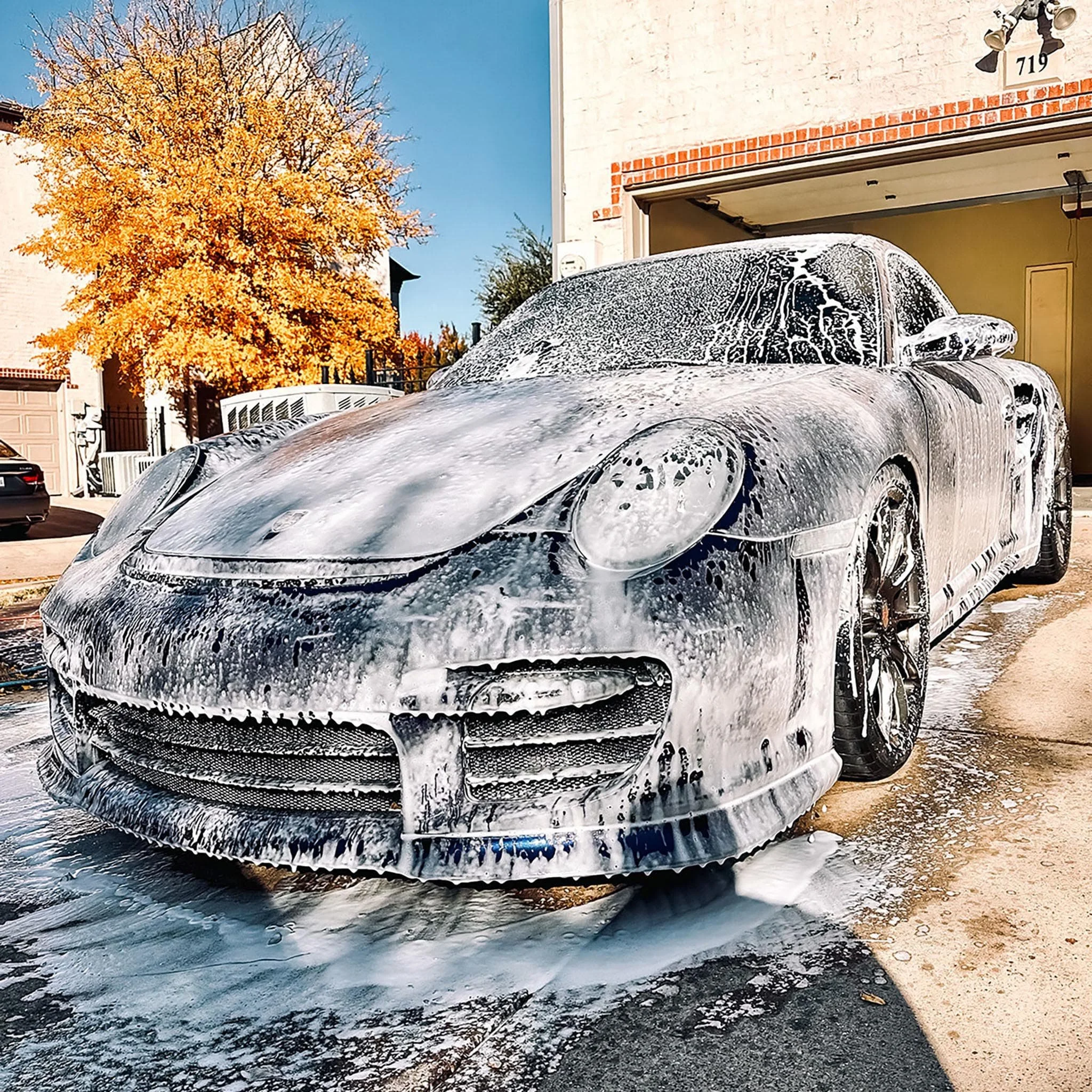 Foam-covered Porsche being washed in a driveway