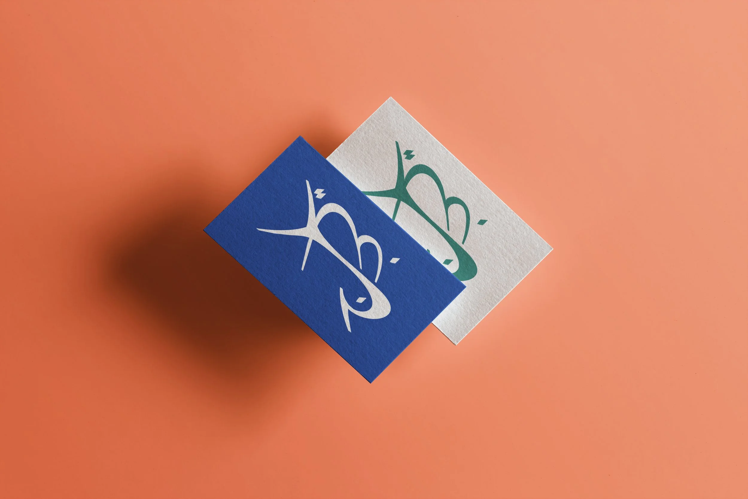 YBJ — deux cartes de visite, l'une en Atlantique et Sable, l'autre en Oasis sur crème, posées sur fond Terre, démonstration des paires chromatiques, mockup par StudioKus