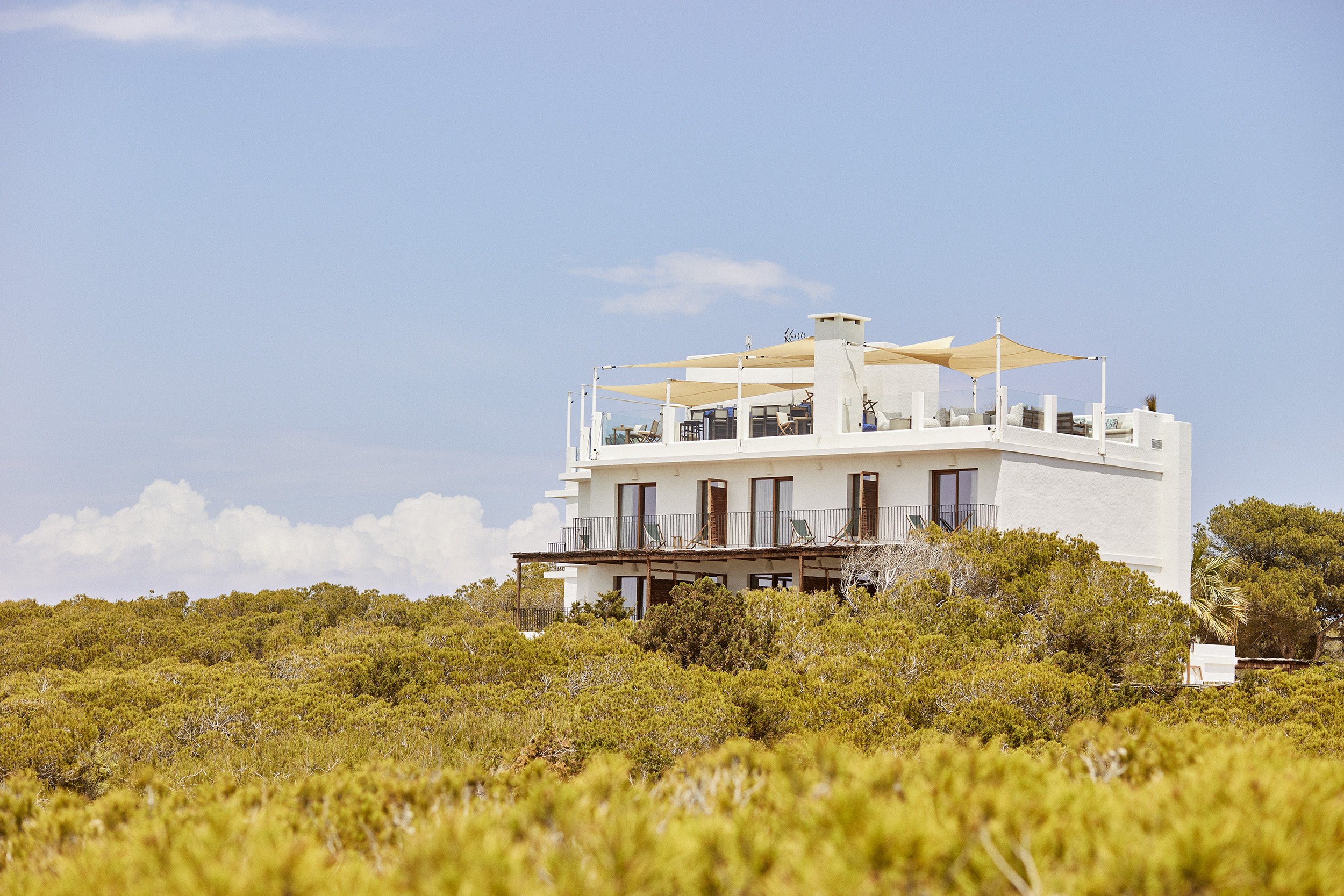 Teranka hotel at dusk seen from above, canvas sails lit against Formentera's pine forest and coastline