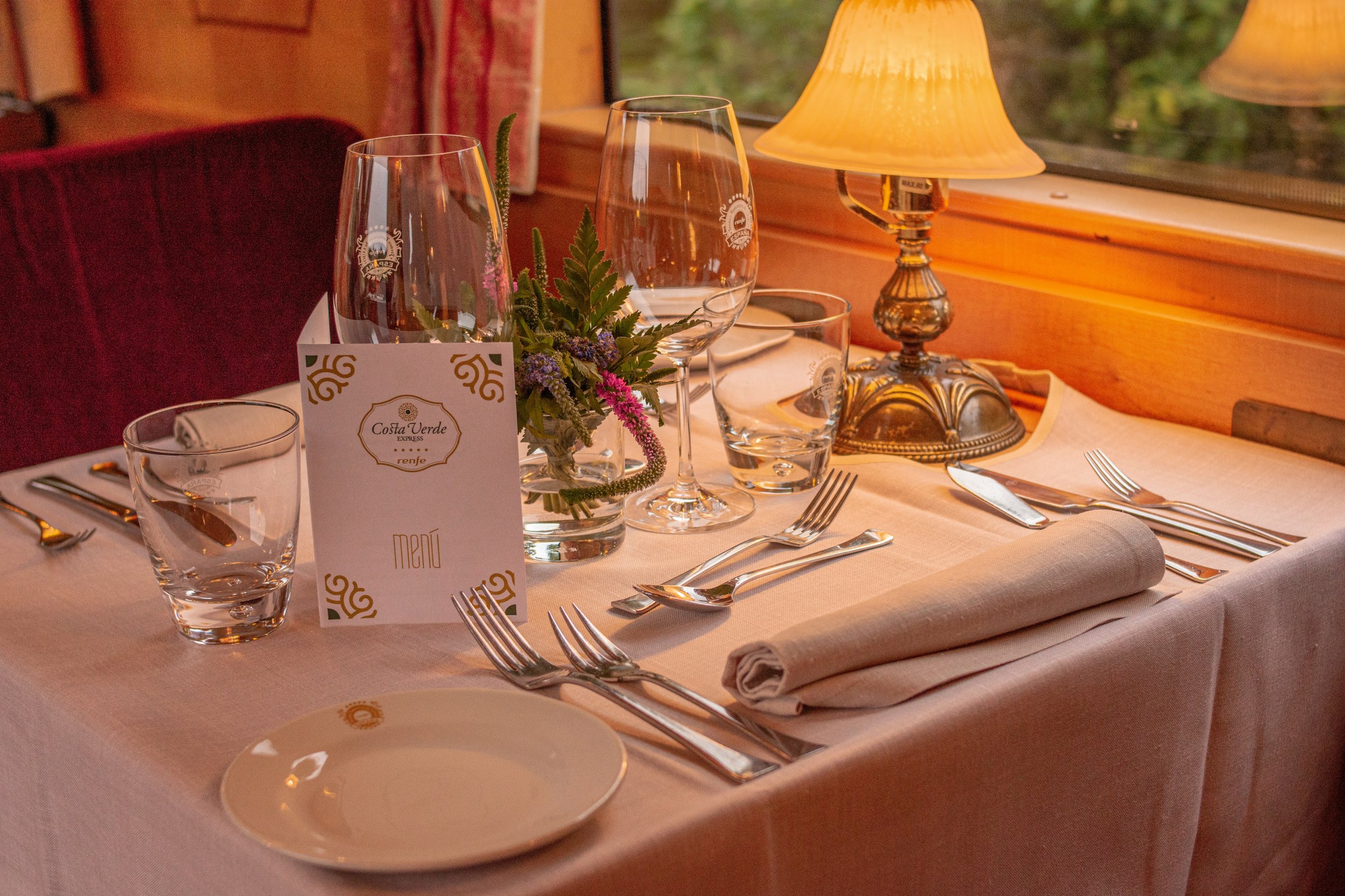 Private luxury train cabin with a table set for dinner, evening light through the window as the landscape passes