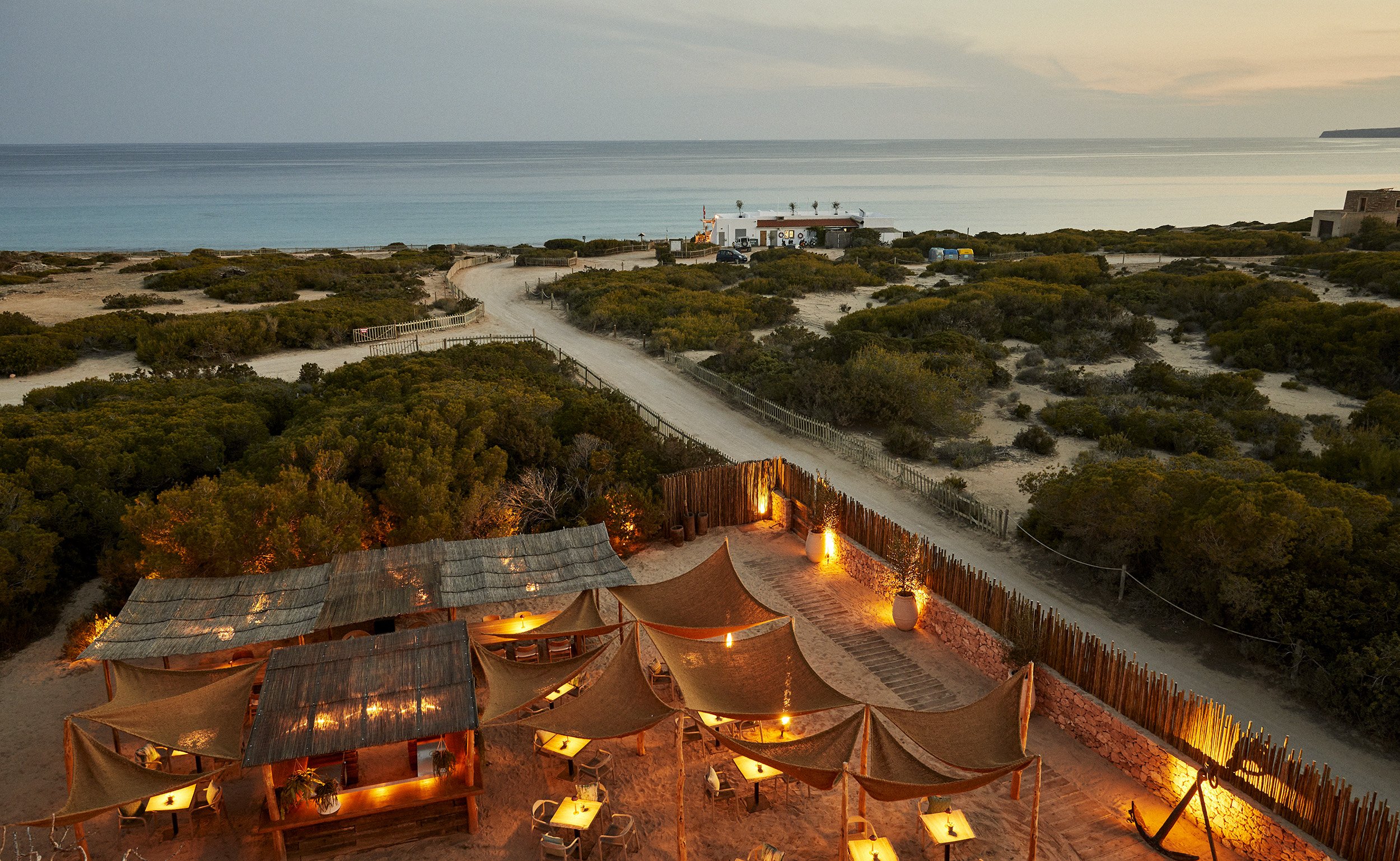 Barefoot luxury terrace overlooking Formentera's coastline, shaded by canvas sails, with the Mediterranean beyond