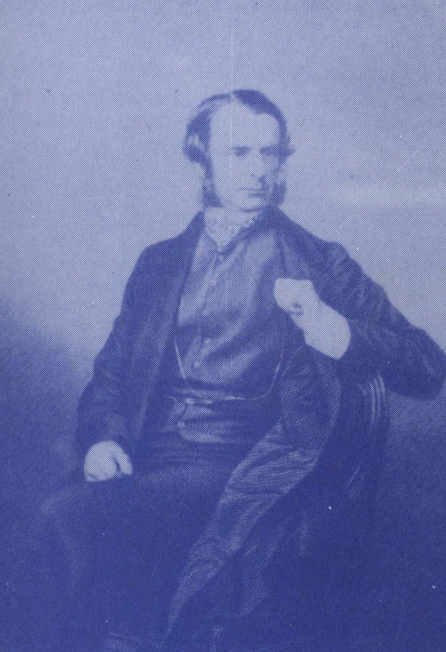 Photographic portrait of Charles Kingsley, seated, in a dark coat with one hand tucked into his jacket