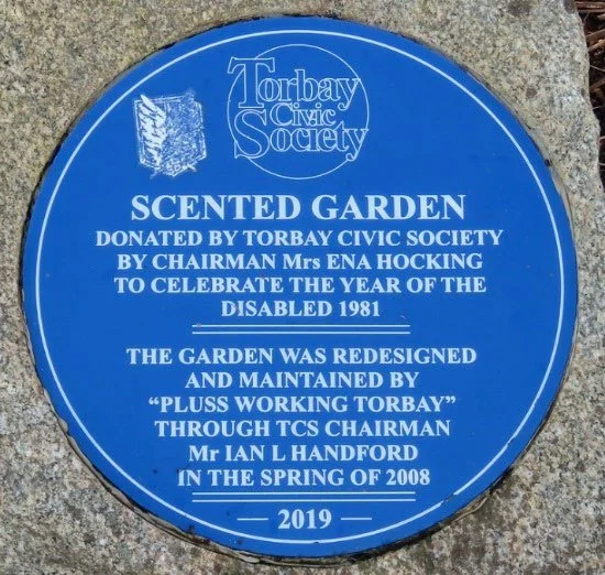 Blue plaque reading Scented Garden, donated by Torbay Civic Society by chairman Mrs Ena Hocking to celebrate the Year of the Disabled 1981, the garden was redesigned and maintained by Pluss Working Torbay through TCS chairman Mr Ian L Handford in the spring of 2008, 2019