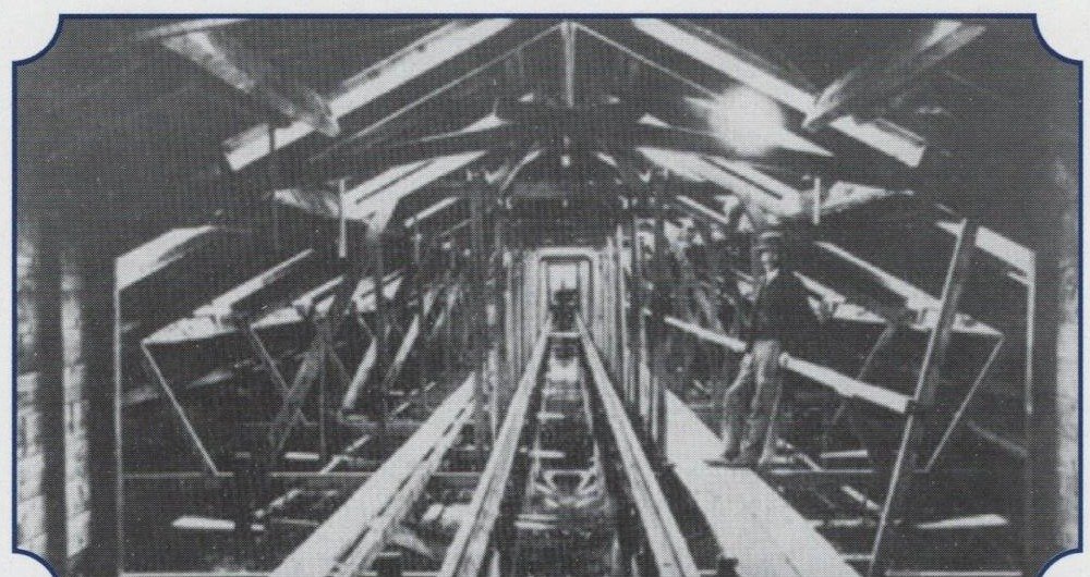 A Victorian photograph of the interior of the covered ship model testing tank at Chelston Cross, Torquay, showing the timber roof trusses and the towing rail running the length of the tank