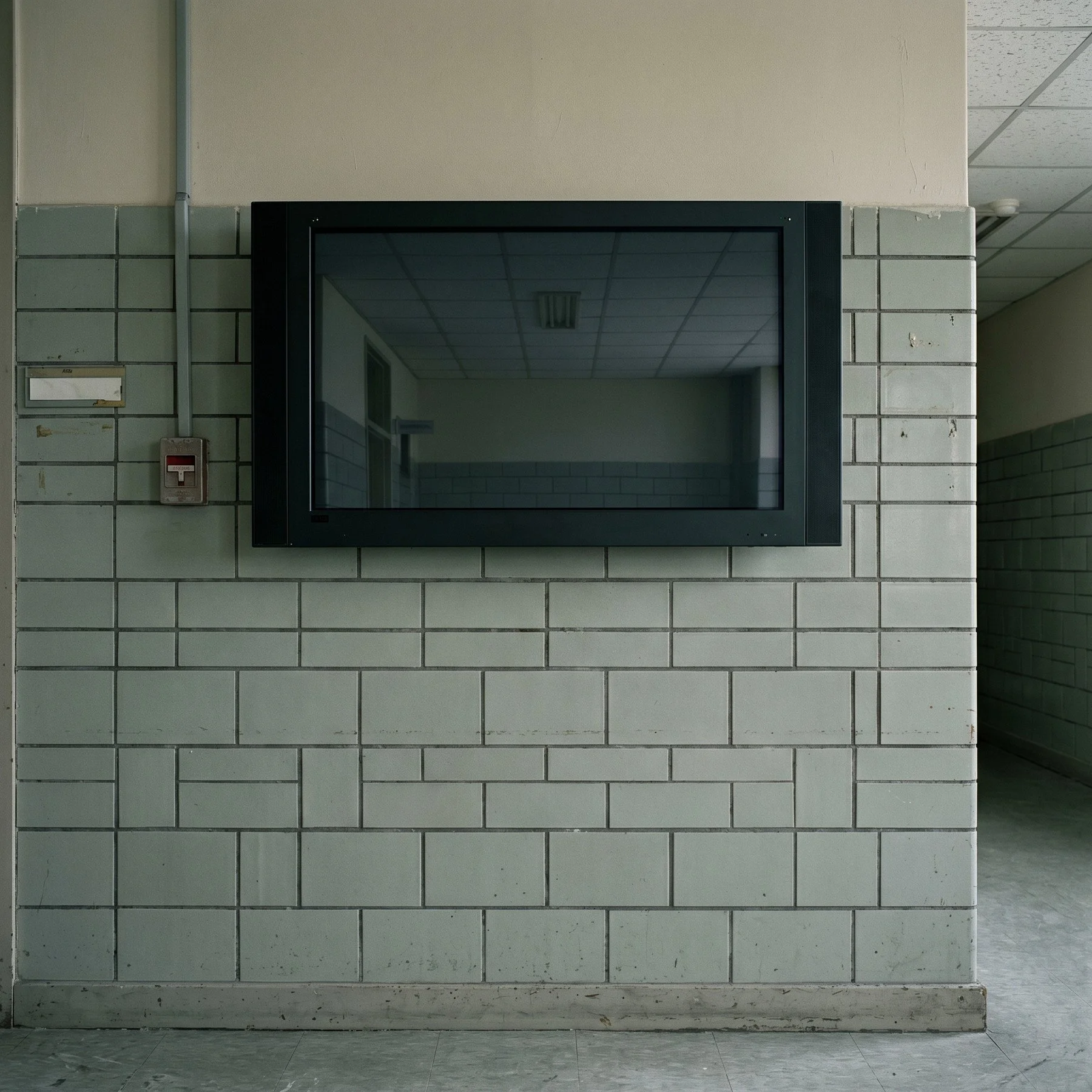 A dark wall-mounted screen reflecting an empty tiled institutional interior.